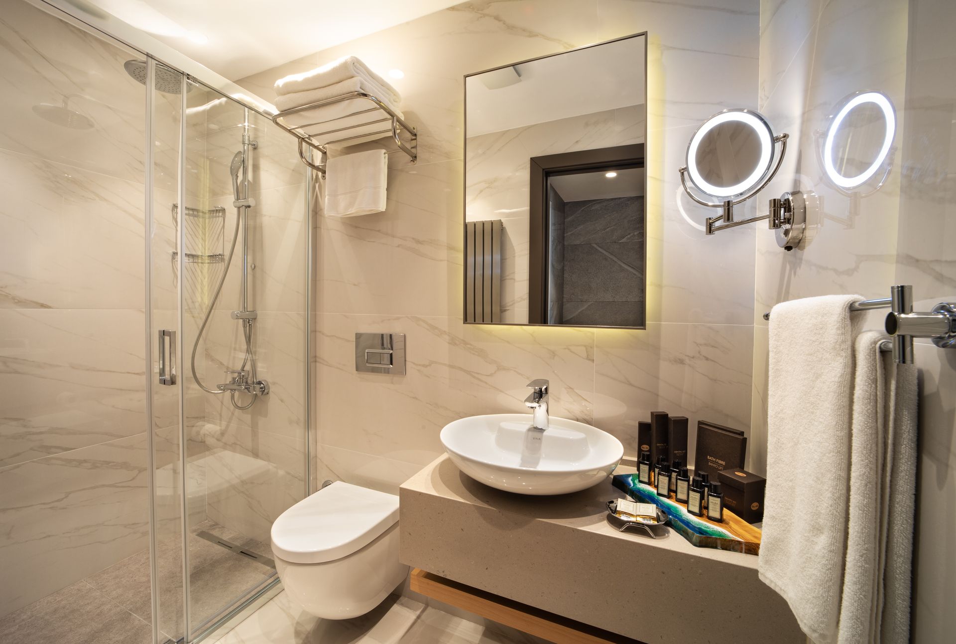 Modern bathroom with shower, toilet, sink, mirror, and lit vanity lights