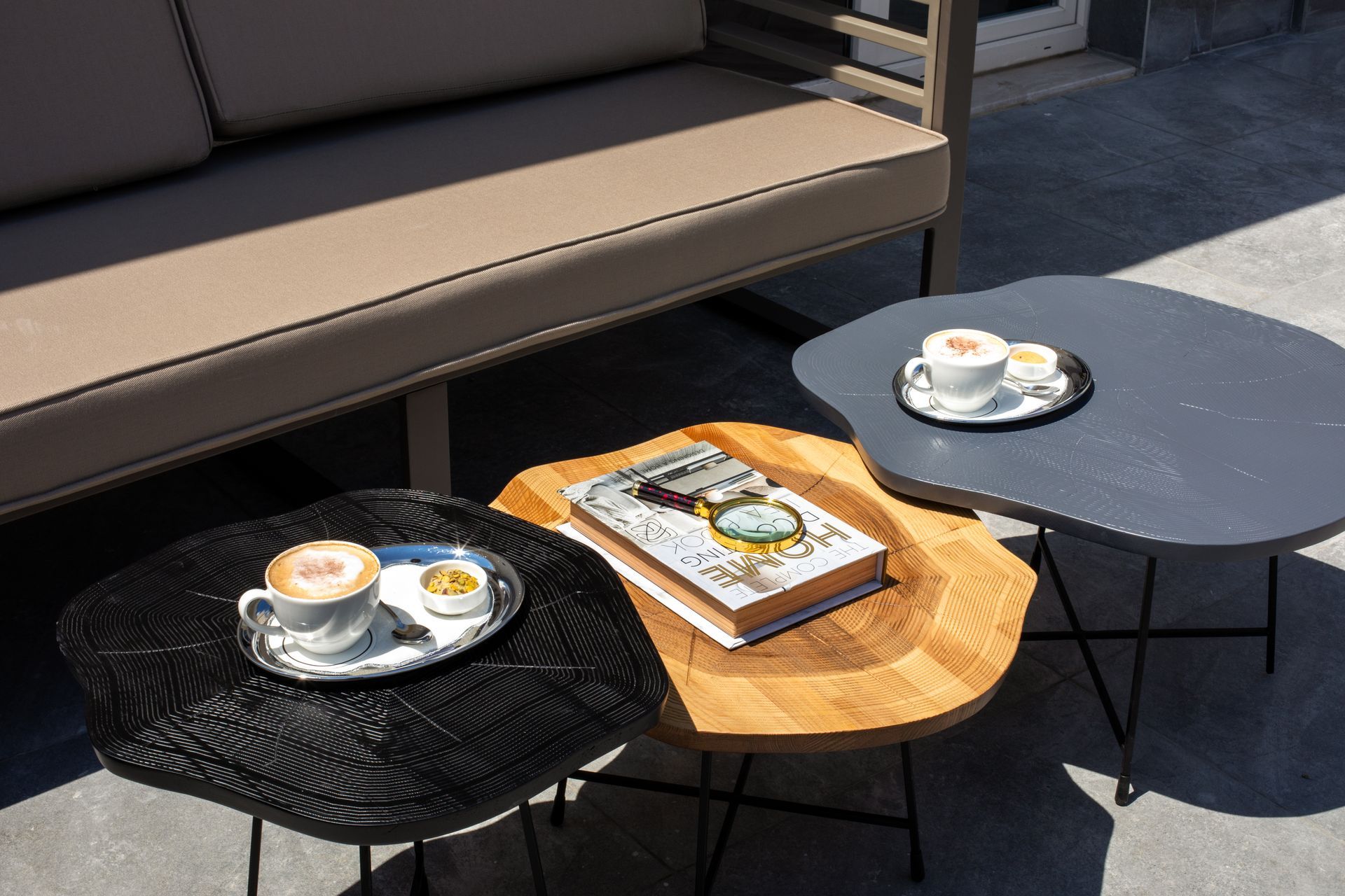 Three outdoor café tables with coffee cups and a book on a sunny patio.