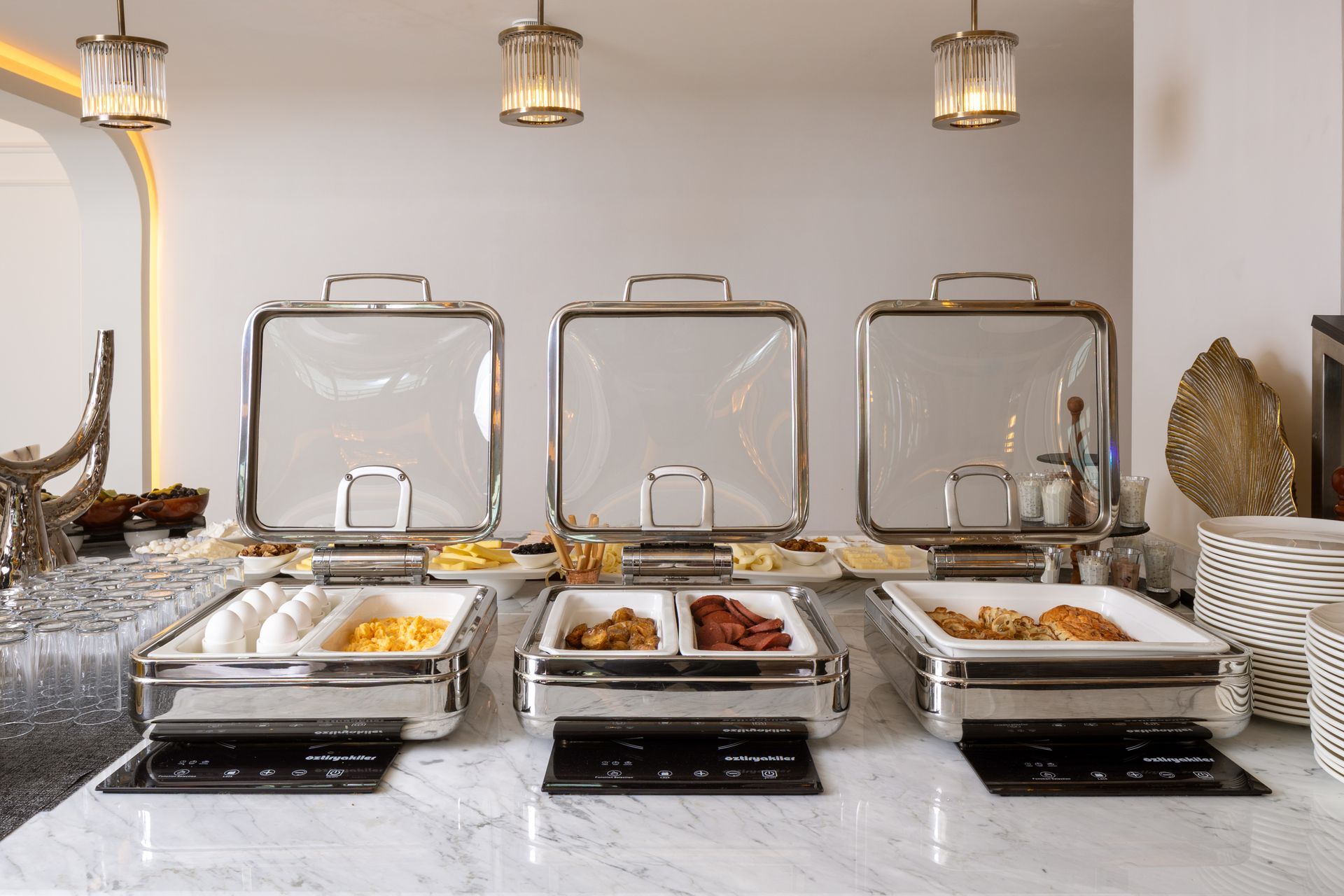 Buffet table with covered serving dishes, plated food, and hanging lanterns in a bright dining room