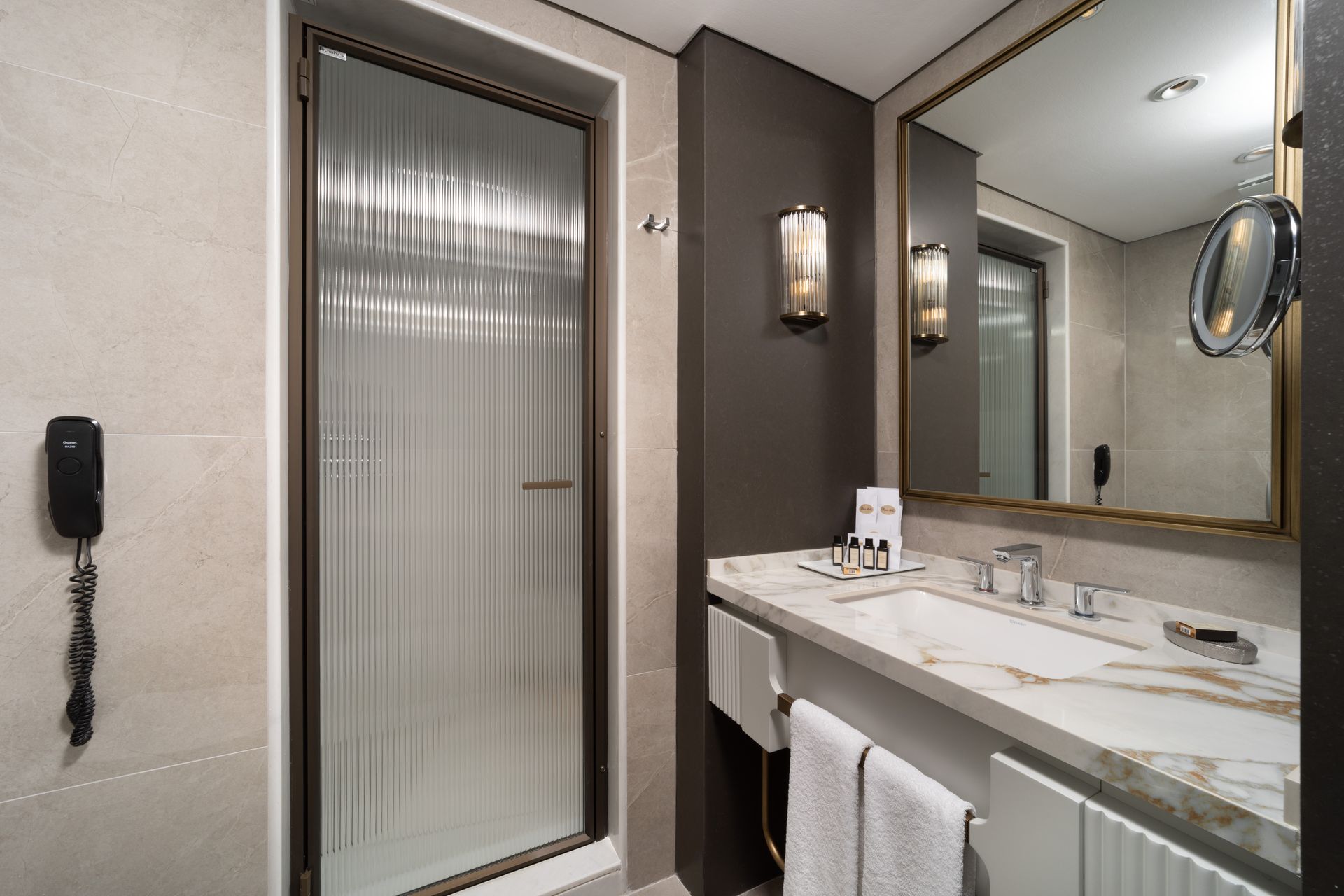 Modern bathroom vanity with mirror, sink, towel, and glass shower door in beige and gray tones