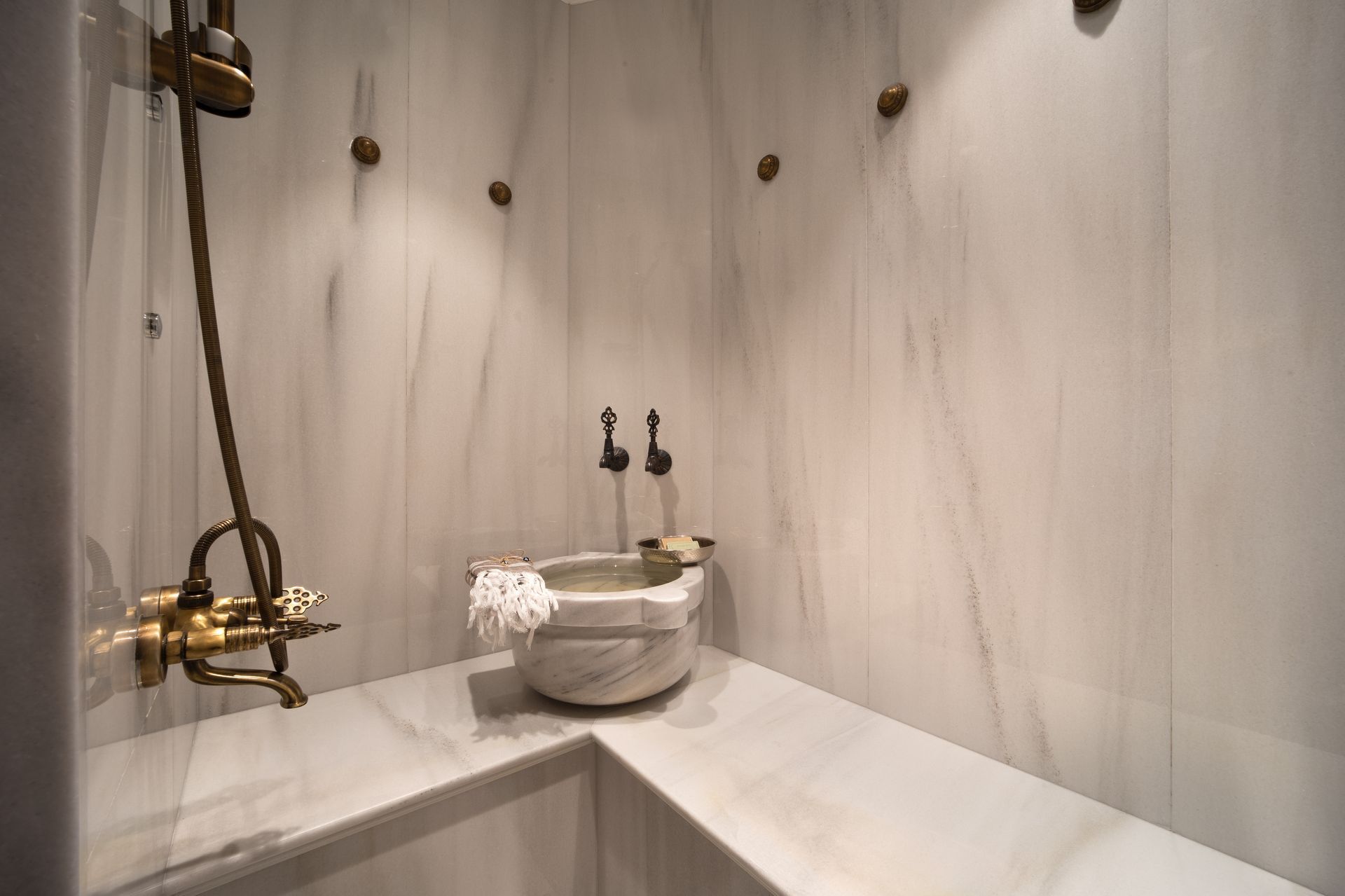 Minimalist shower area with white tile bench, round stone basin, and brass fixtures on marble walls
