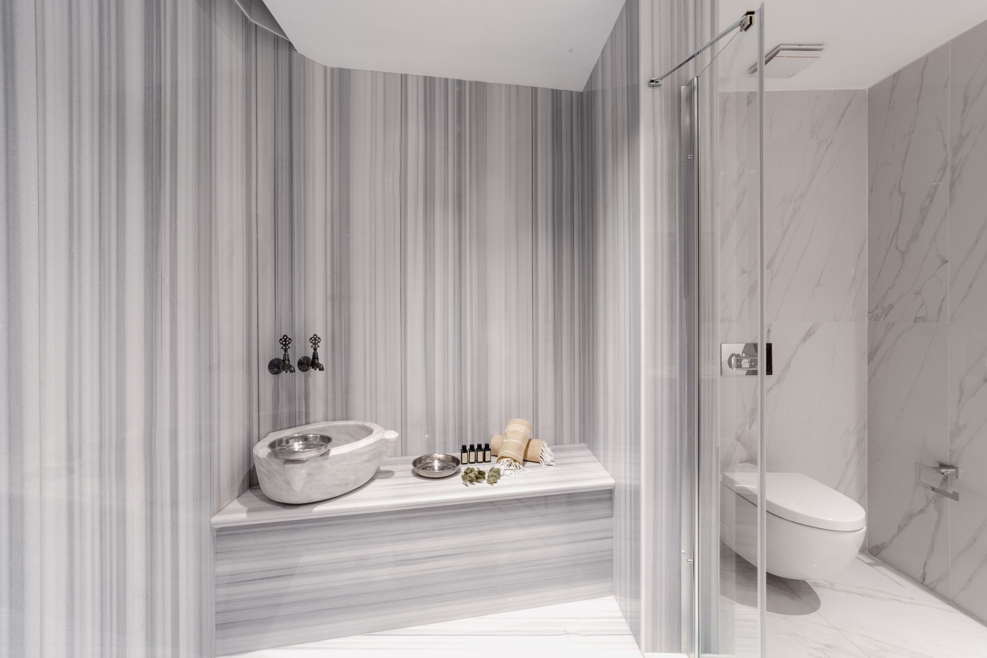 Modern marble bathroom with striped wallpaper, freestanding tub, glass shower, and vanity with bowl sink
