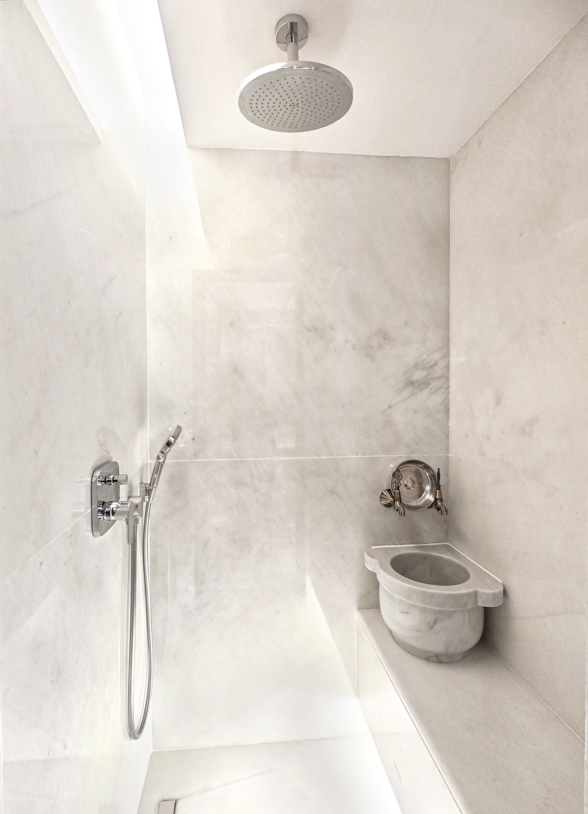 Small white tiled shower room with wall-mounted toilet and handheld showerhead