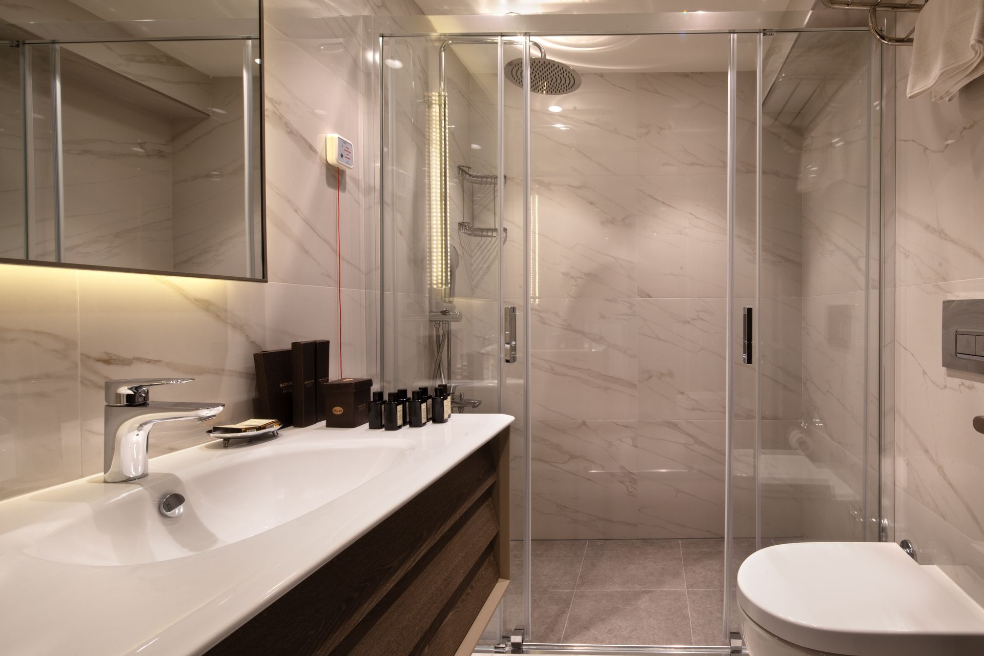 Modern bathroom with double sinks, large mirror, glass shower, and white marble tile.