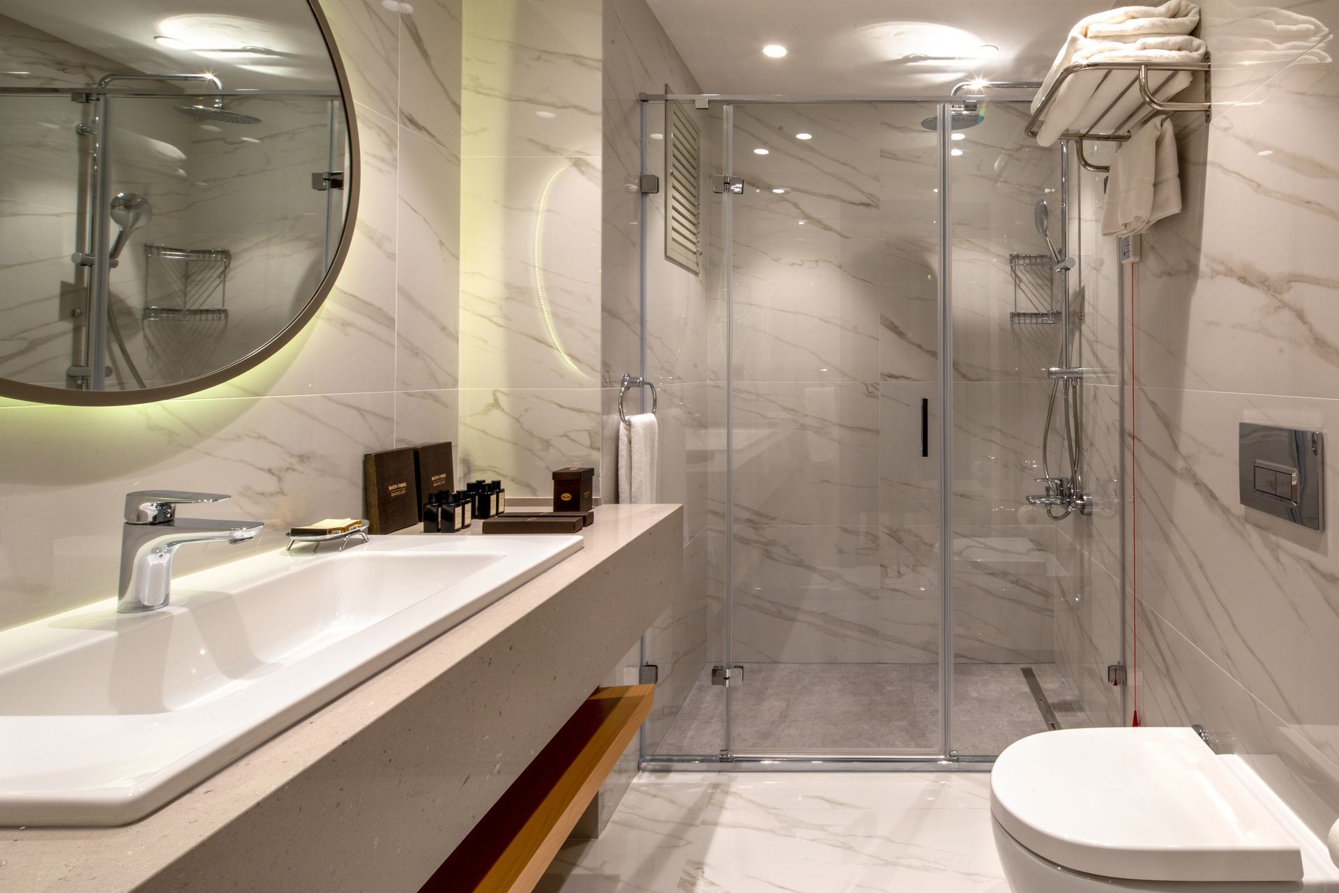 Modern bathroom with marble walls, glass shower, white sink, and toilet