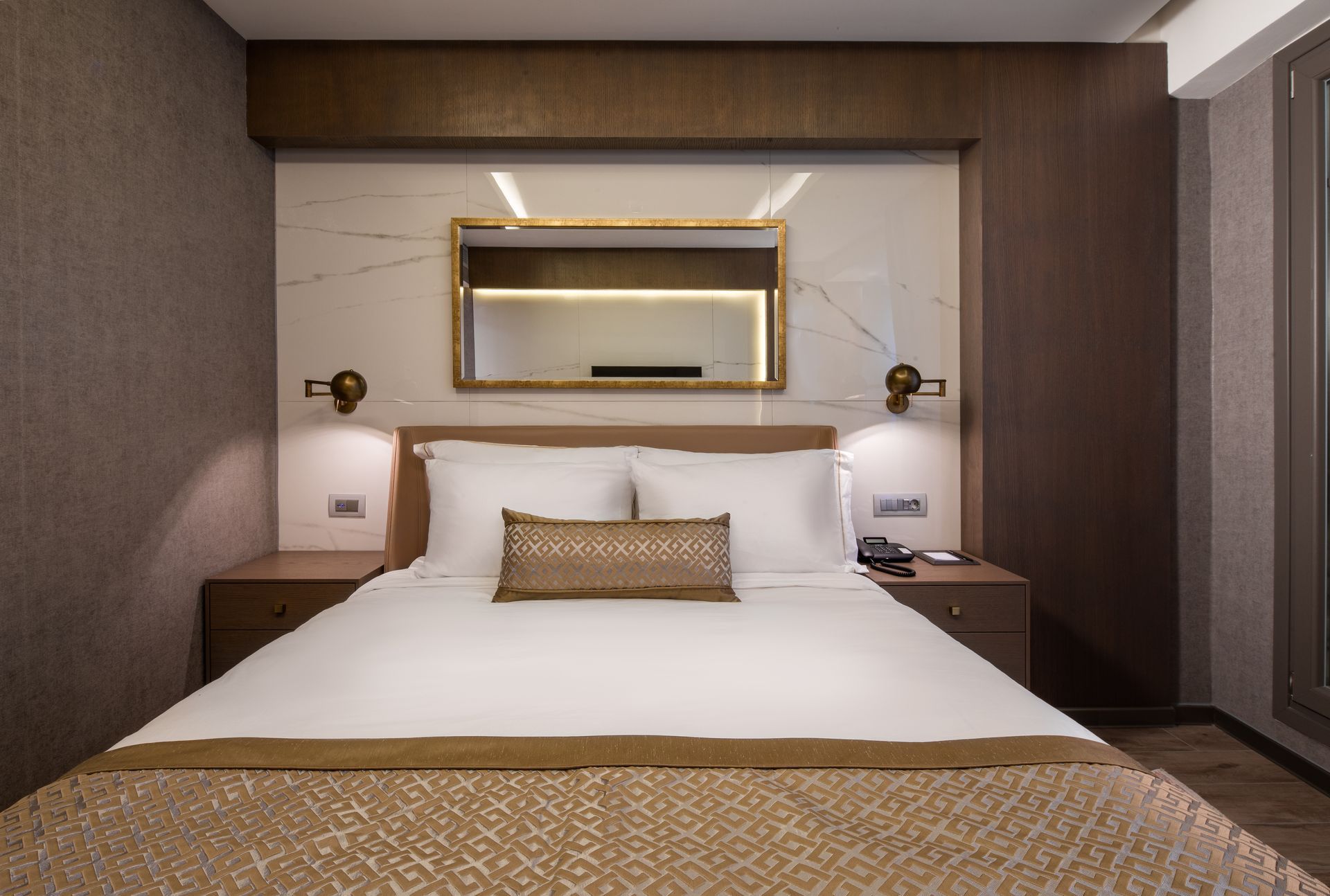 Modern hotel room with a neatly made bed, bedside lamps, and a wall mirror above the headboard
