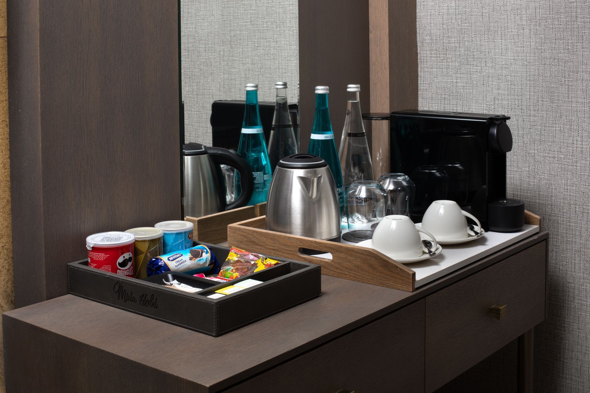 Coffee and tea station with cups, bottles, snacks, and a kettle on a countertop