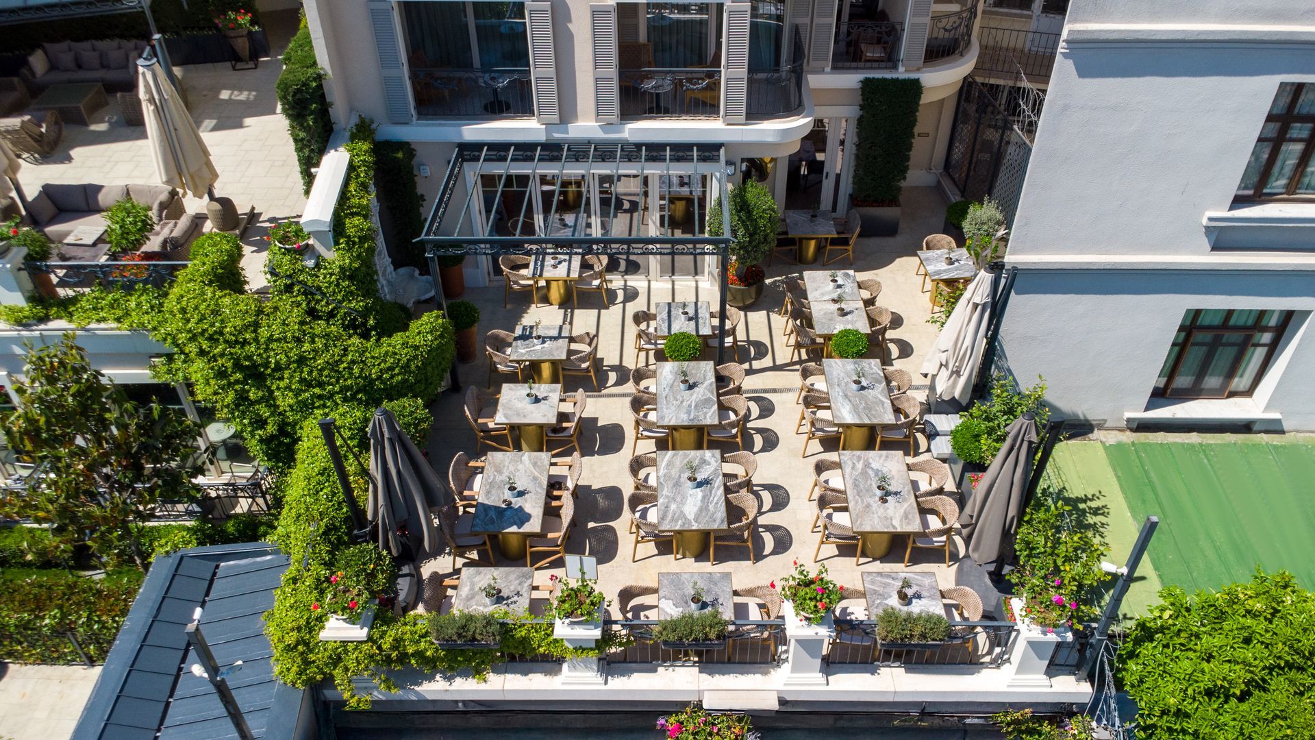 Aerial view of a rooftop café patio with many tables, chairs, and umbrellas beside a building.