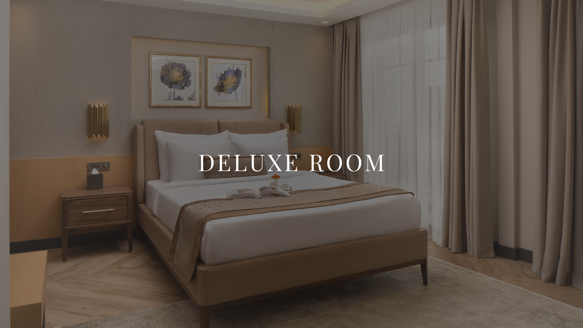 Elegant beige hotel bedroom with a king bed, bedside tables, wall art, and floor-to-ceiling curtains; “DELUXE ROOM” text.