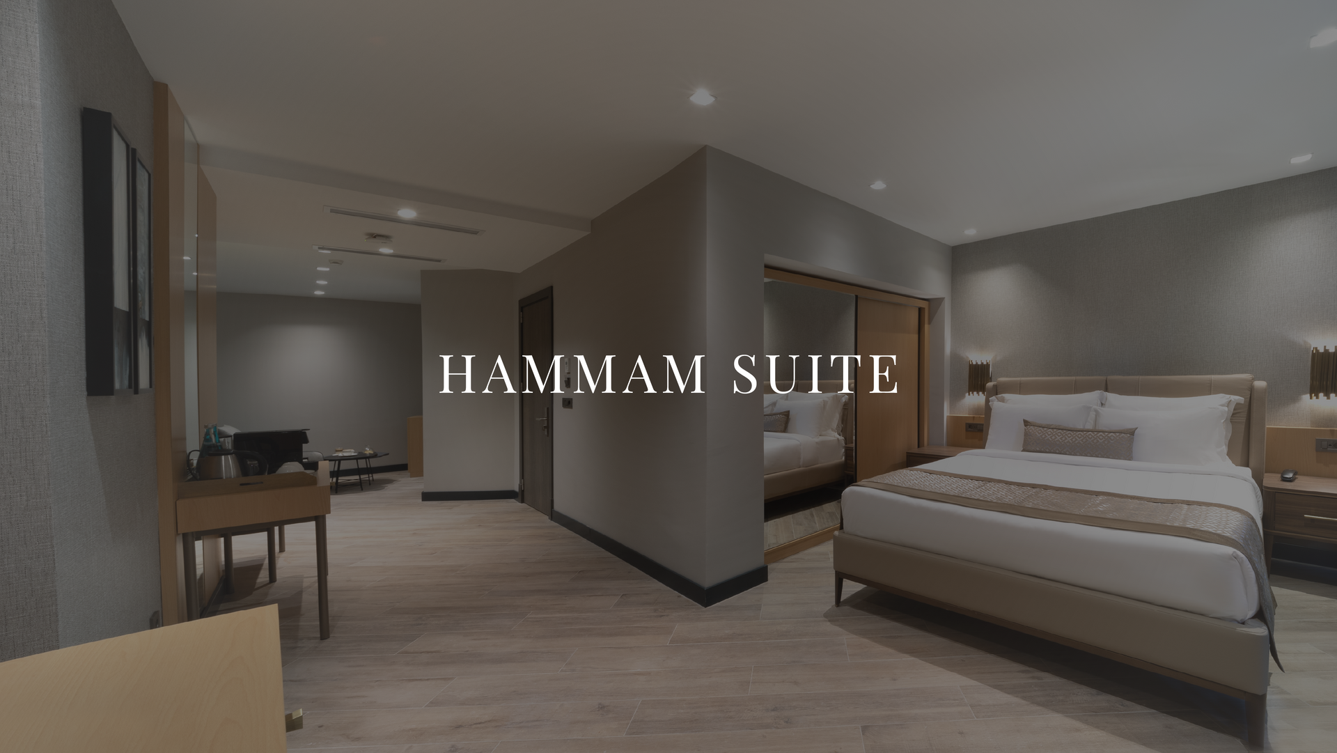 Modern hotel suite with two beds, desk, and hallway; text reads “HAMMAM SUITE.”