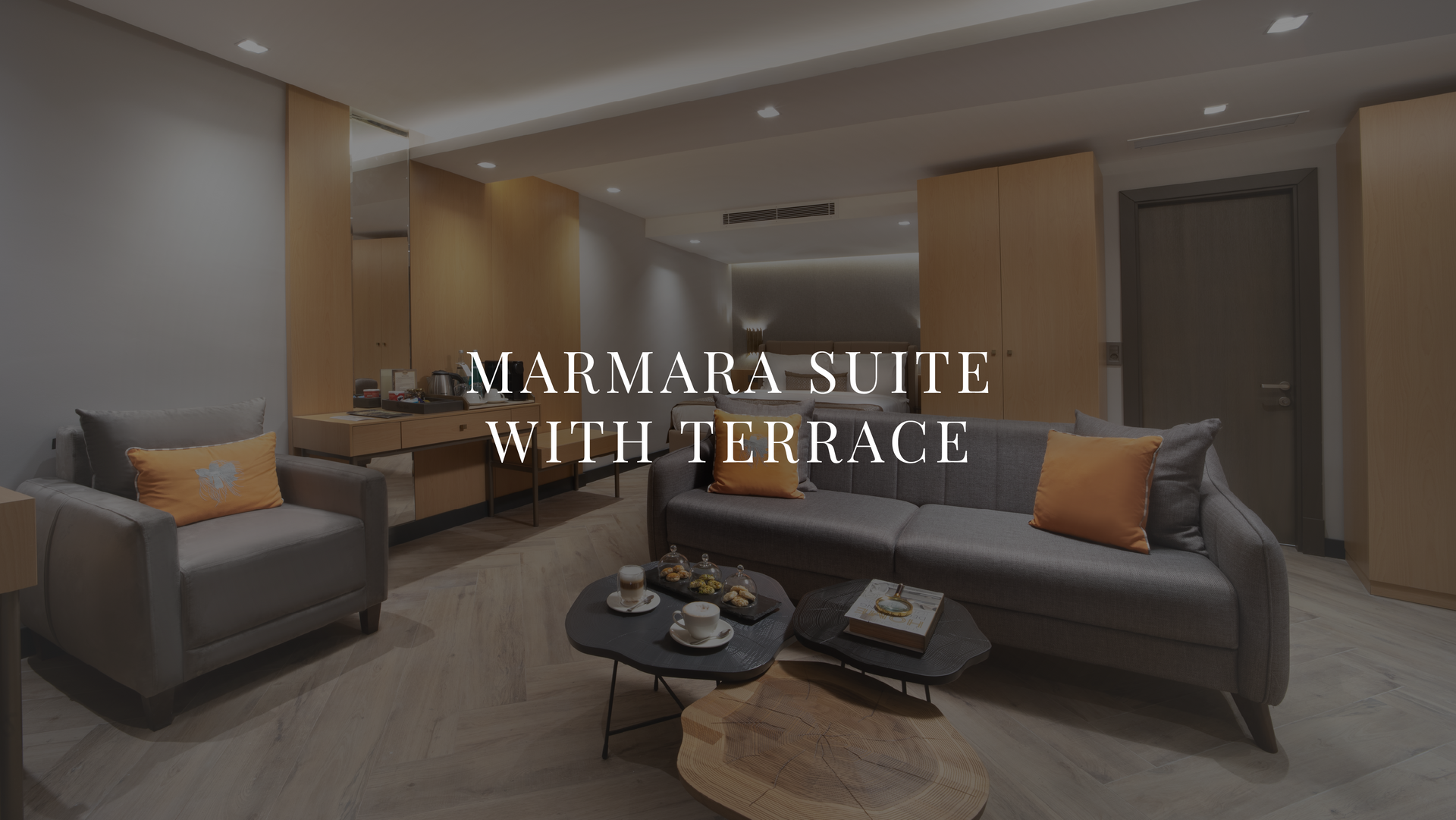 Modern suite living room with gray sofas, orange pillows, and a terrace view