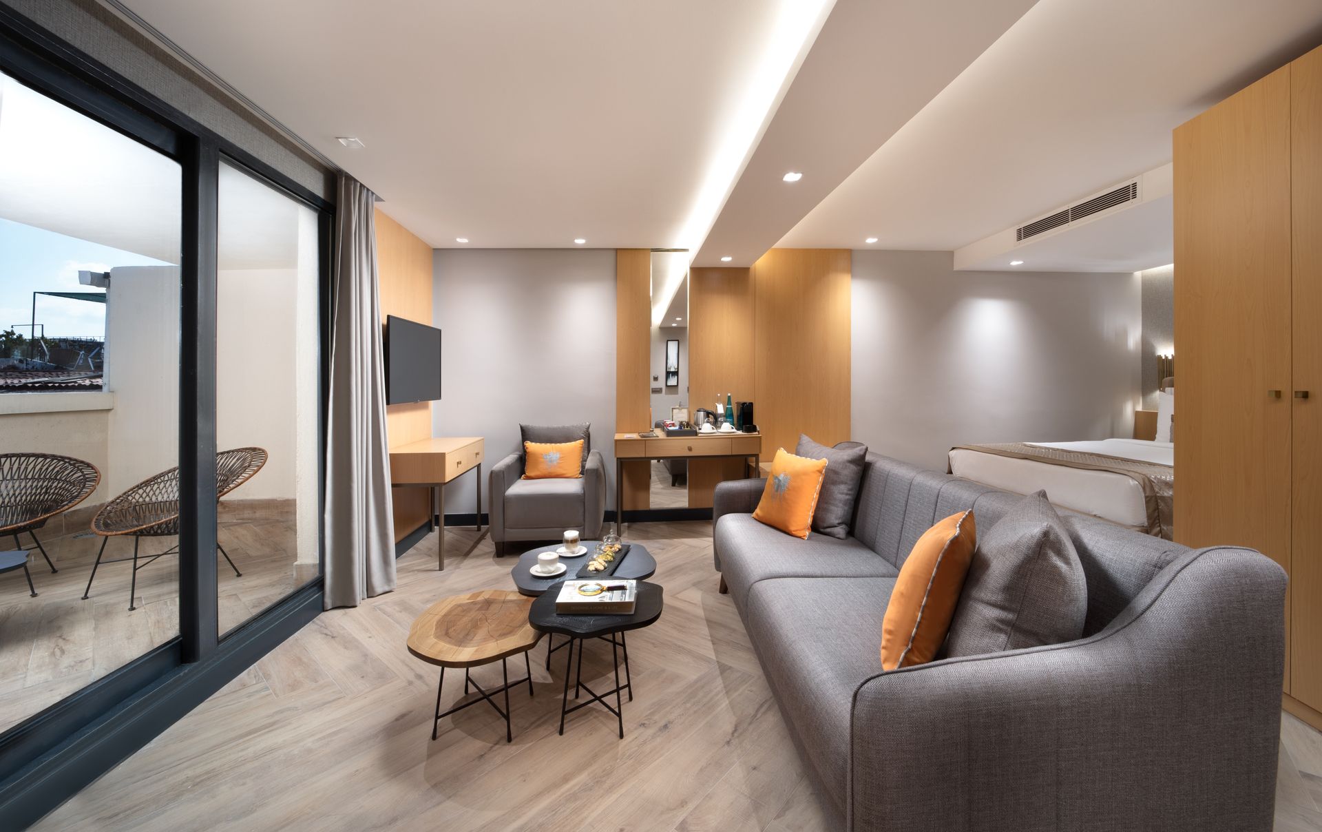 Mula Hotel | Modern hotel suite with gray sofa, orange pillows, balcony, and light wood furniture.