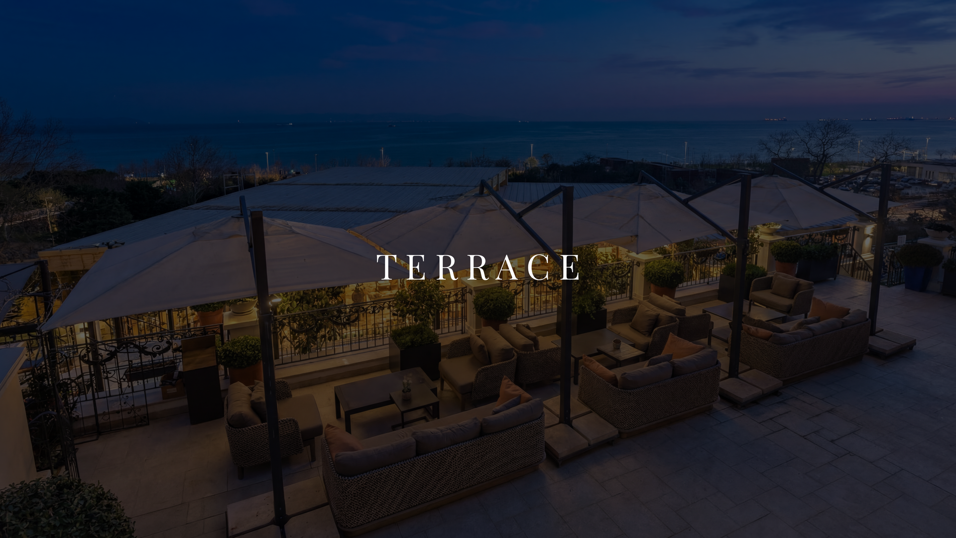 Rooftop terrace lounge at dusk with canopy seating and city lights in the background