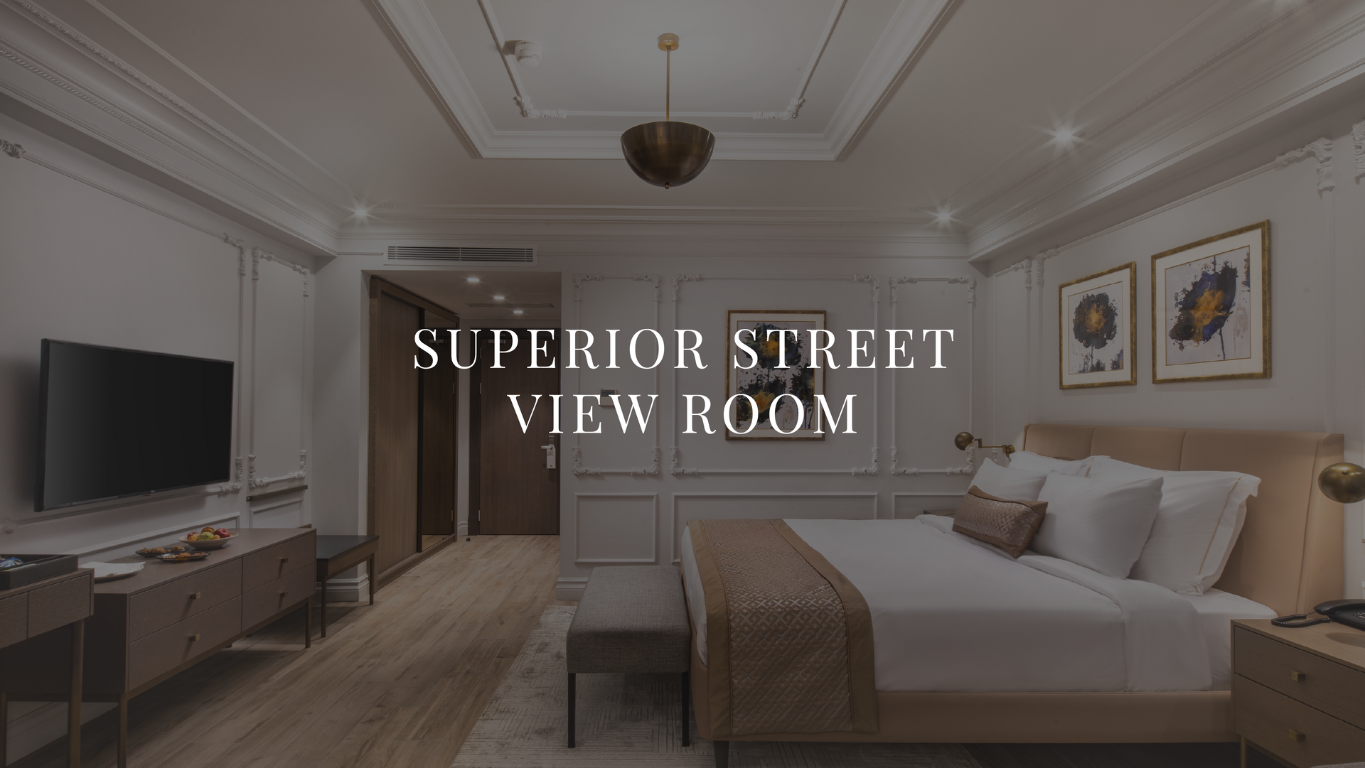 Elegant hotel room with king bed, chandelier, wall-mounted TV, and text reading “Superior Street View Room”