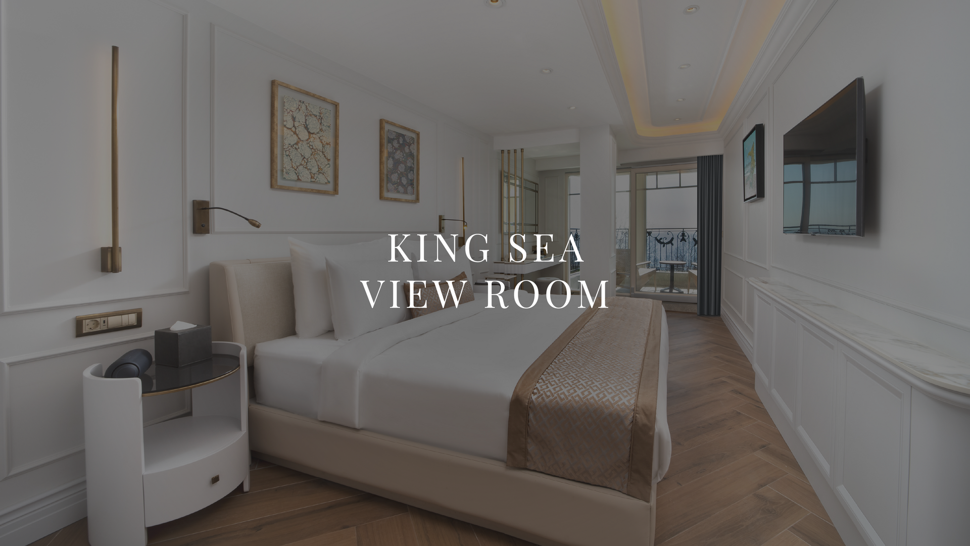 Bright bedroom suite with king bed, ocean-view seating, and wall-mounted TV in a modern hotel room.