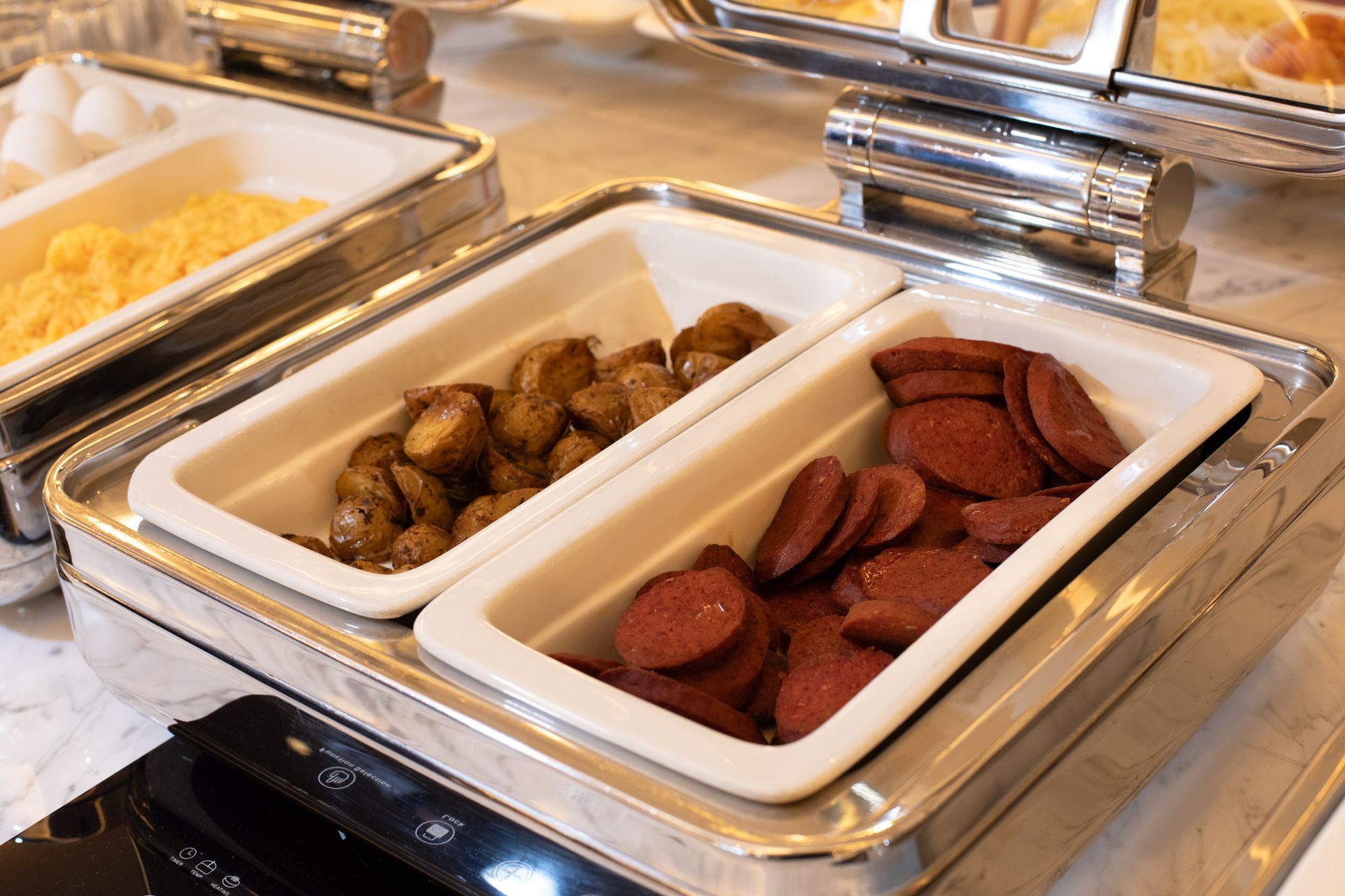 Mula Hotel | Breakfast buffet: scrambled eggs, roasted potatoes, and sliced sausage in warming trays.