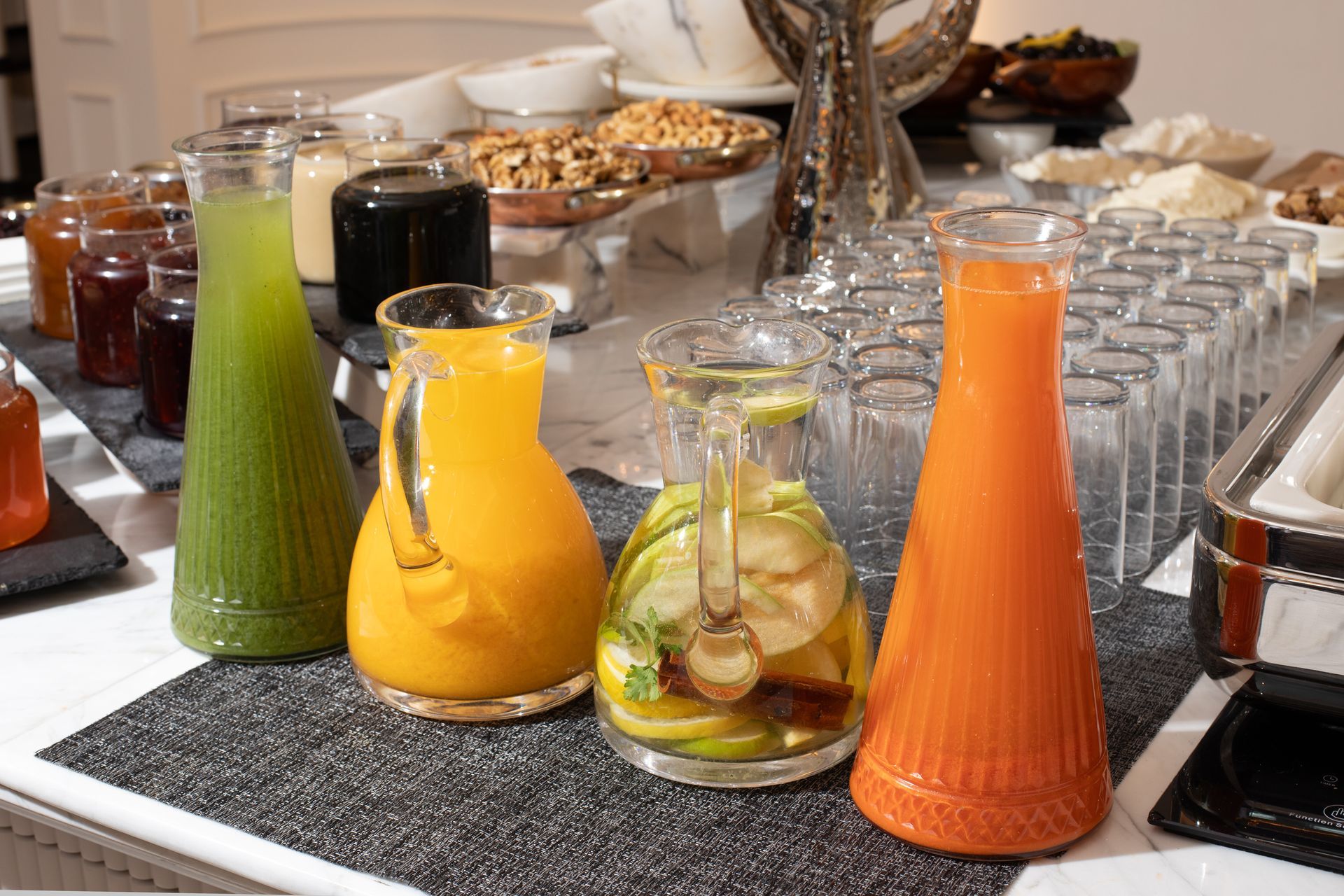 Mula Hotel | Buffet with various juices in clear glass pitchers; oranges, green, and a fruit infused.
