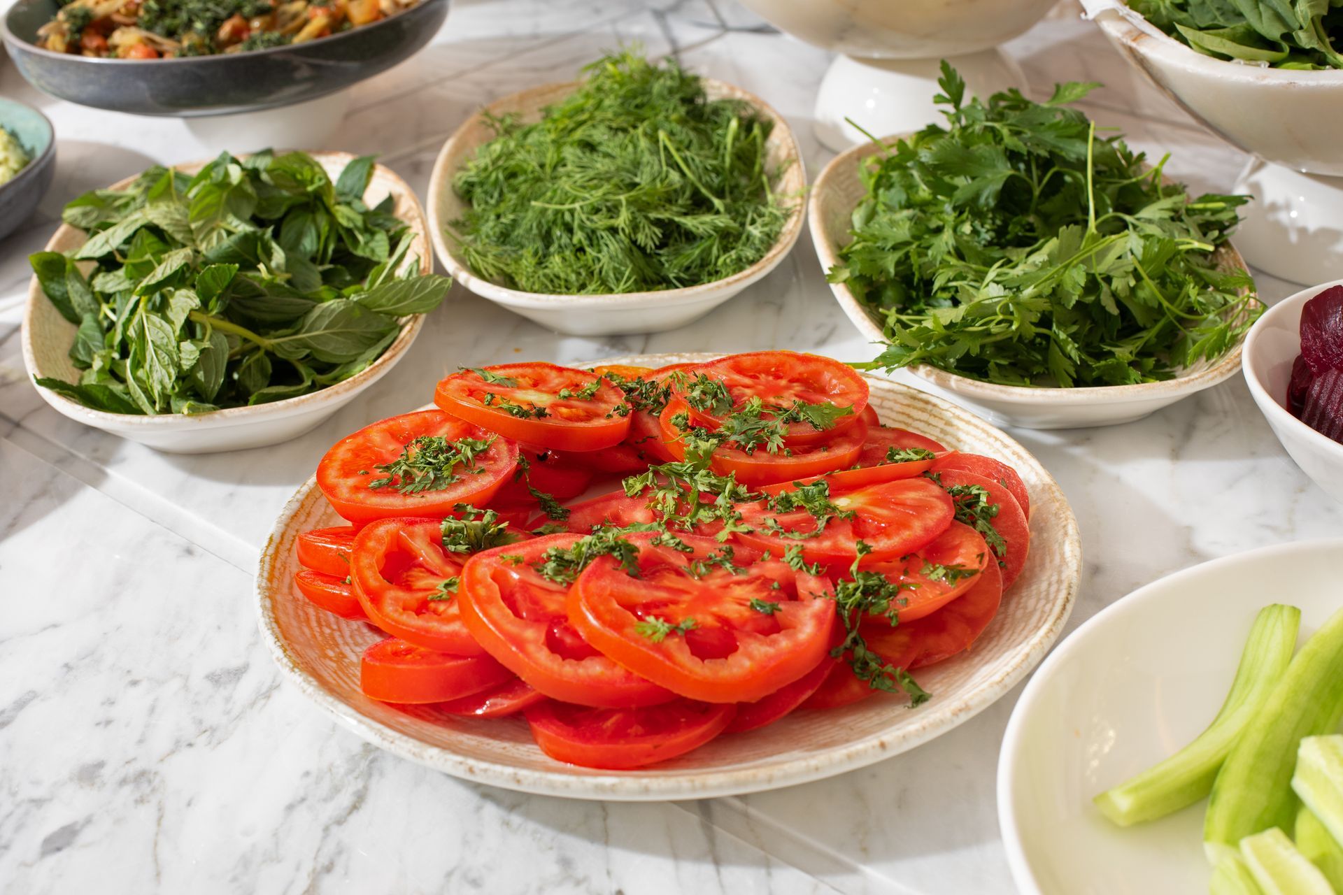 Mula Hotel | Tomato slices garnished with herbs, surrounded by bowls of greens and other vegetables.