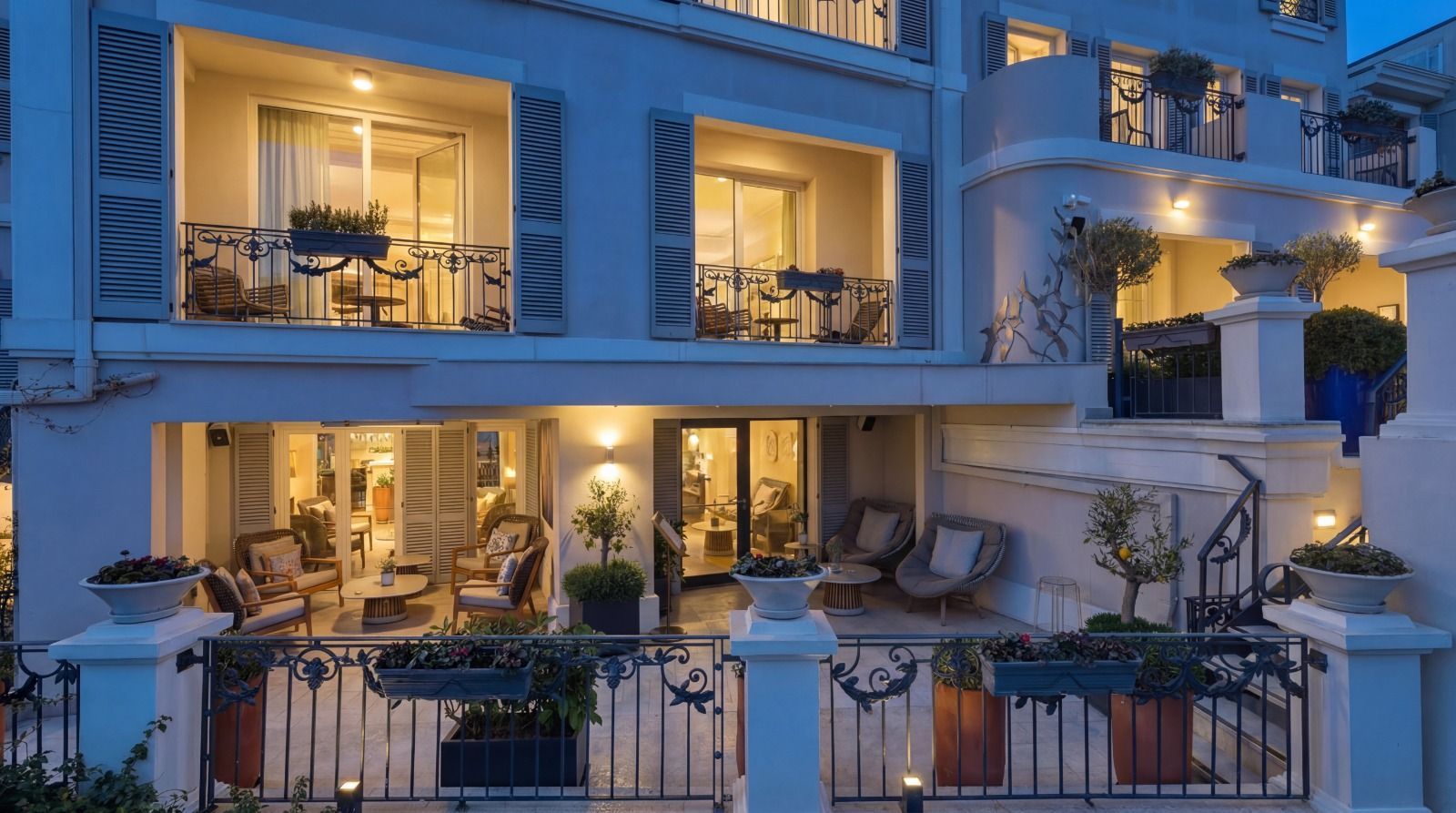 Balconies of a warmly lit luxury hotel at dusk, with white railings and patio furniture.
