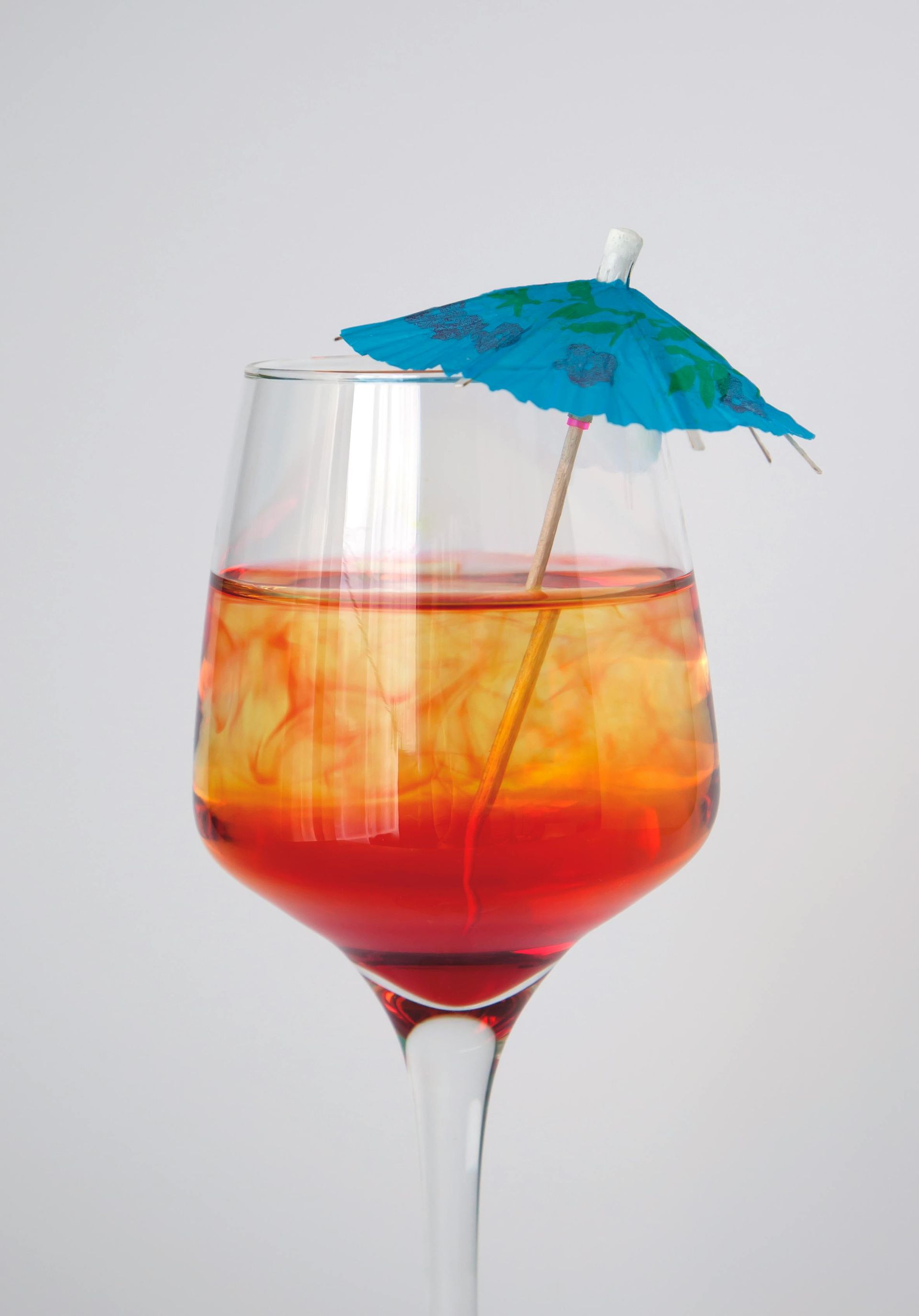 Mula Hotel | Cocktail in a stemmed glass with red and yellow layers, topped with a blue paper umbrella.