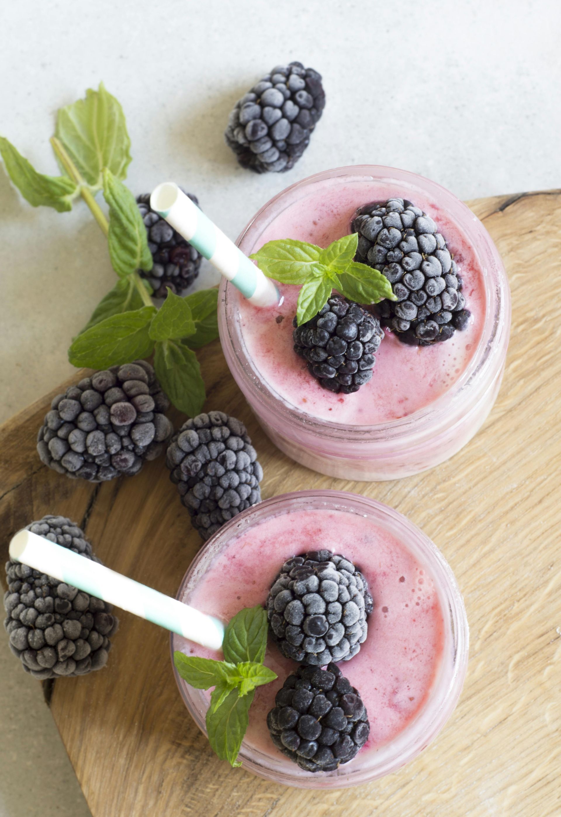Mula Hotel |Two pink smoothies in glass jars, garnished with blackberries and mint on a wooden board.