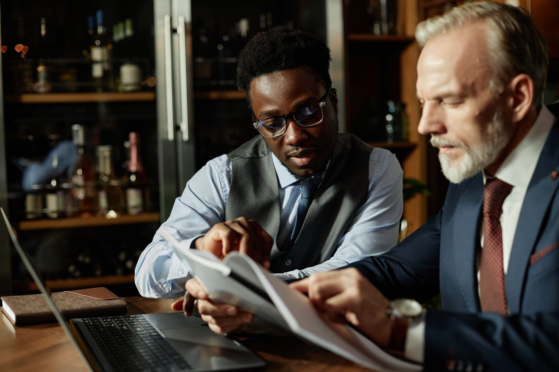 Two people reviewing documents at a laptop in a dimly lit office or café