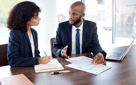 Two professionals discussing documents at a desk in a bright office