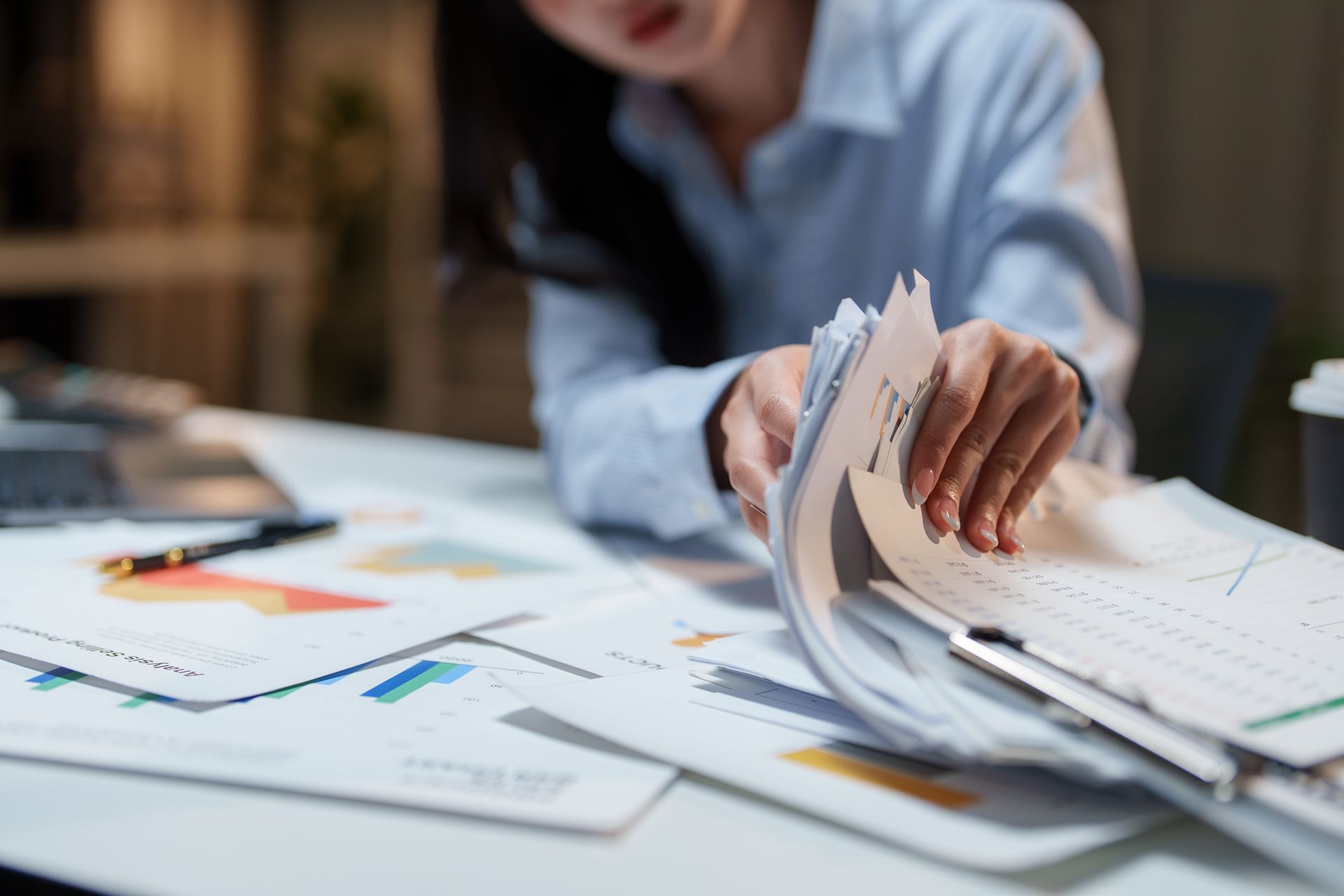 Person sorting paper documents at a desk with charts and graphs