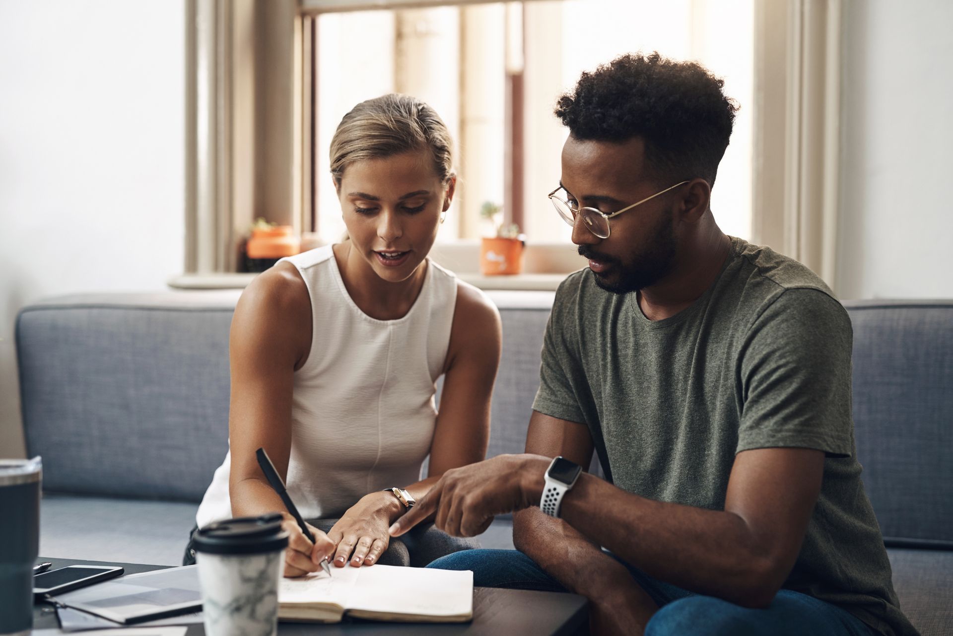 Two people reviewing notes on a couch with a laptop and coffee cup nearby