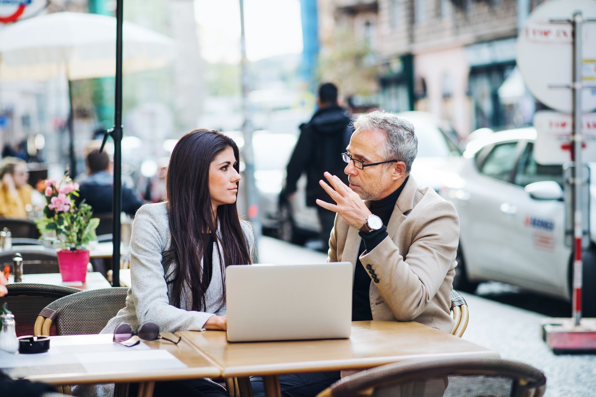 Two people talking at an outdoor café with a laptop on the table