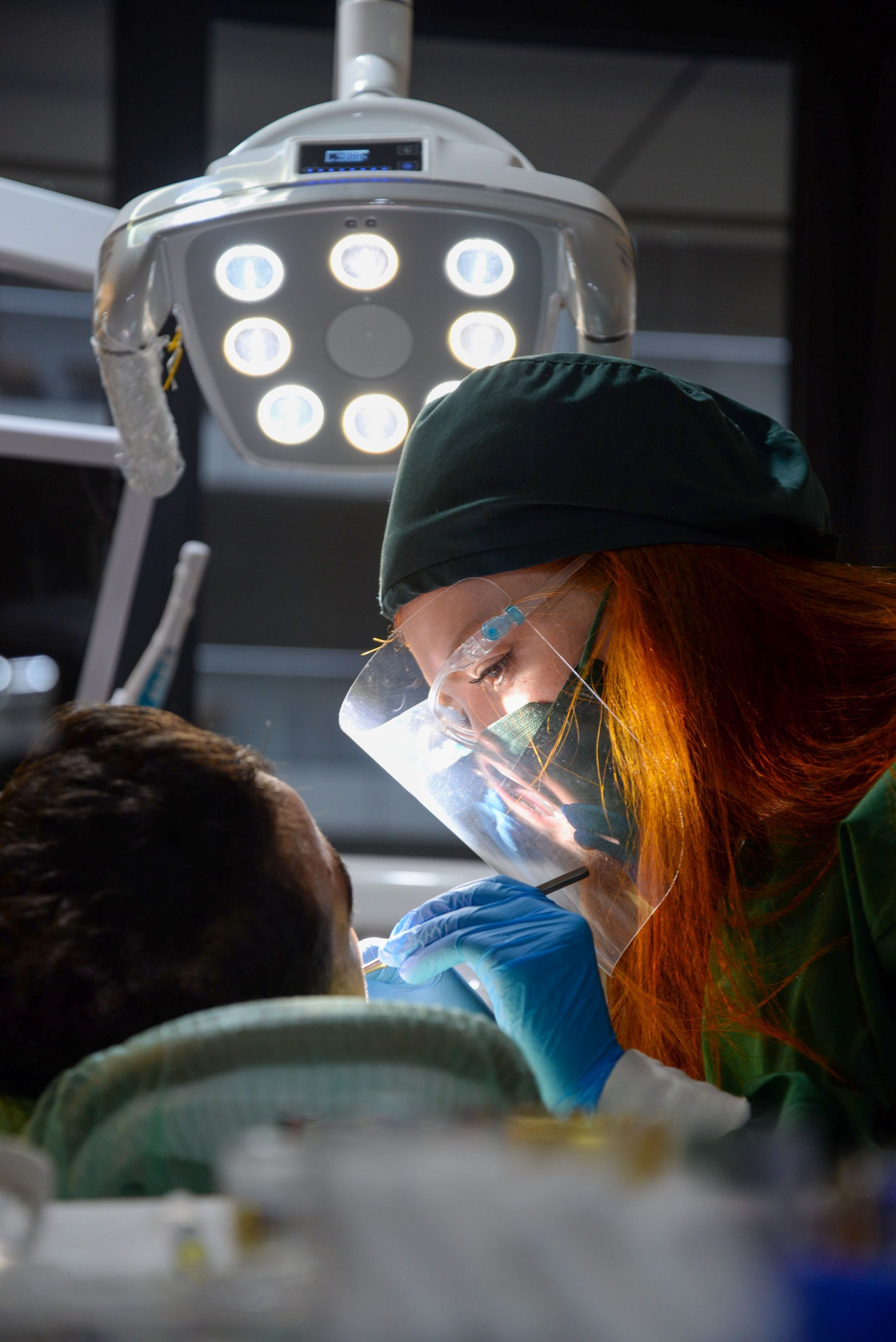 Surgeon in green scrubs and mask working under bright operating room lights
