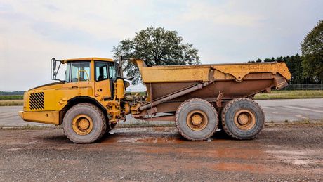 Yellow dump truck on a dirt road with an orange trailer at sunset