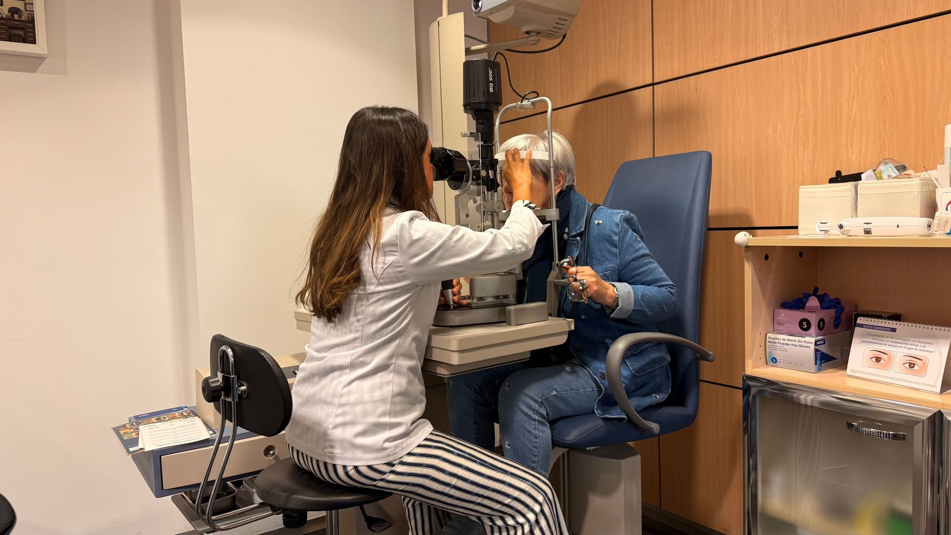 Eye exam with a clinician adjusting equipment for a seated patient in a clinic room