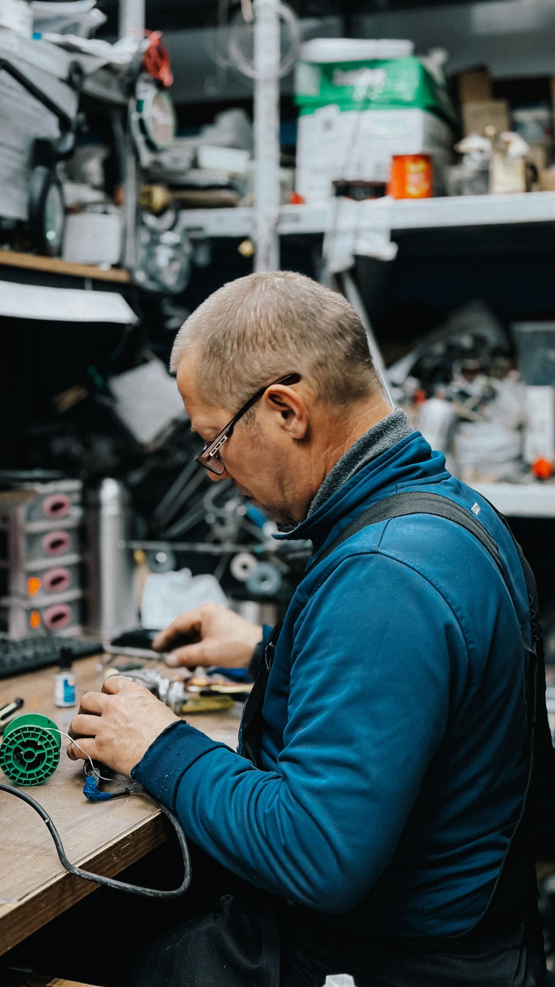 Person working at a cluttered desk in a workshop, focused on assembling a small electronic device.