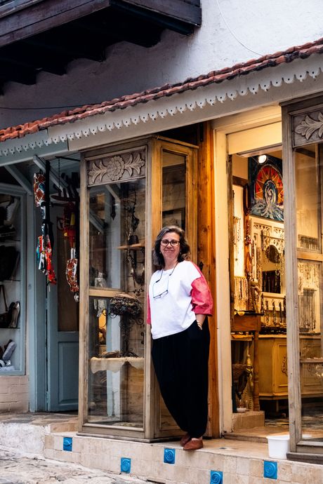 Woman standing in a shop doorway on a sidewalk, wearing a white shirt and black pants, with pink bag over shoulder