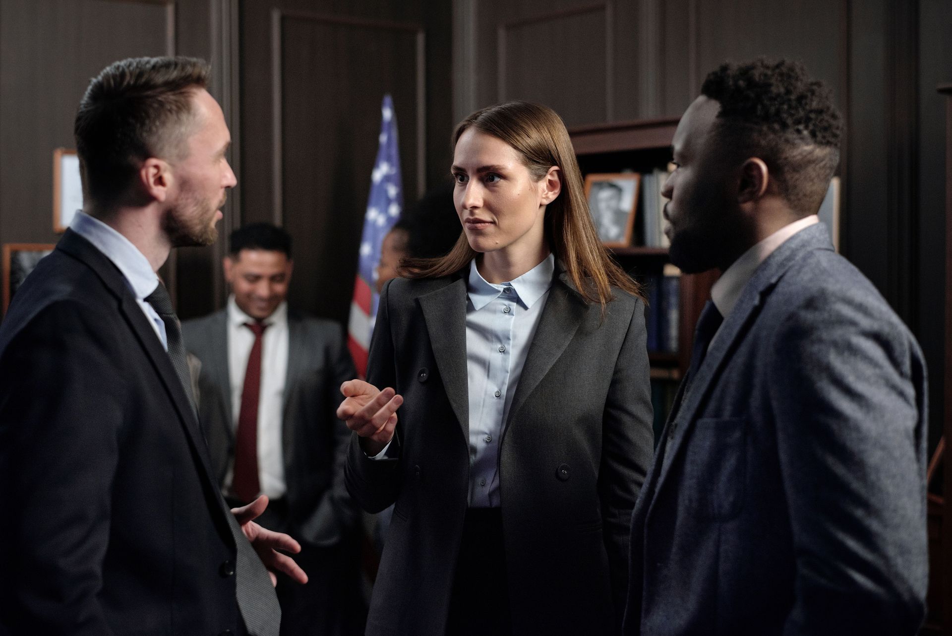 Three professionals in suits converse in a dimly lit office