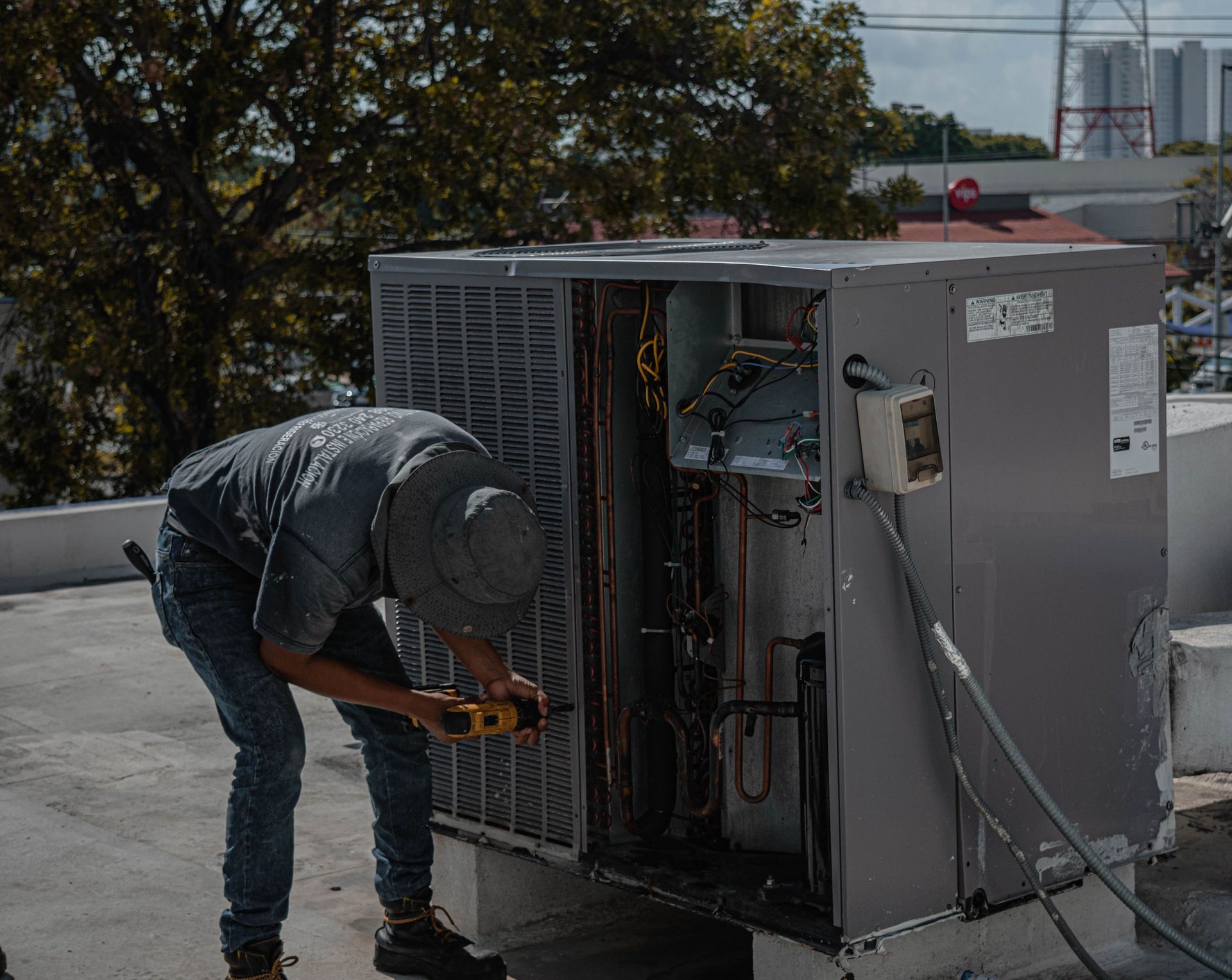 Worker repairing rooftop HVAC unit with tools on a flat roof