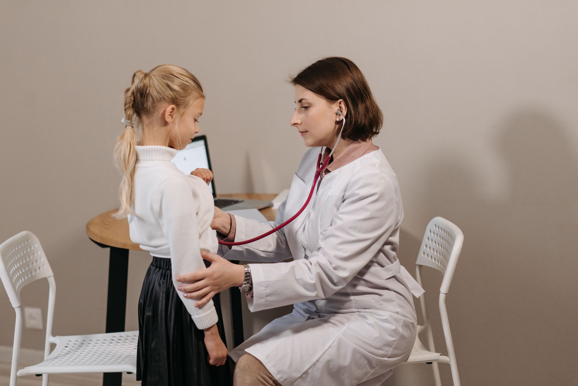 Doctor examining a young child with a stethoscope in a clinic room