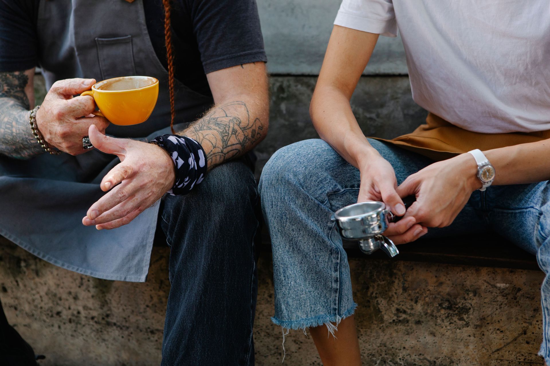 Two people sitting on a stone ledge, one holding a yellow cup and the other a small camera.