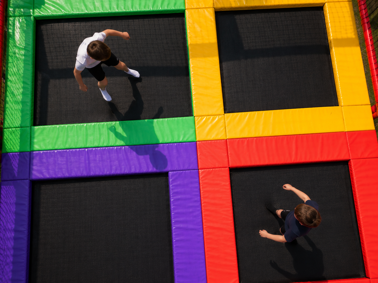 People jumping on colorful square trampolines with green, yellow, purple, and red frames.