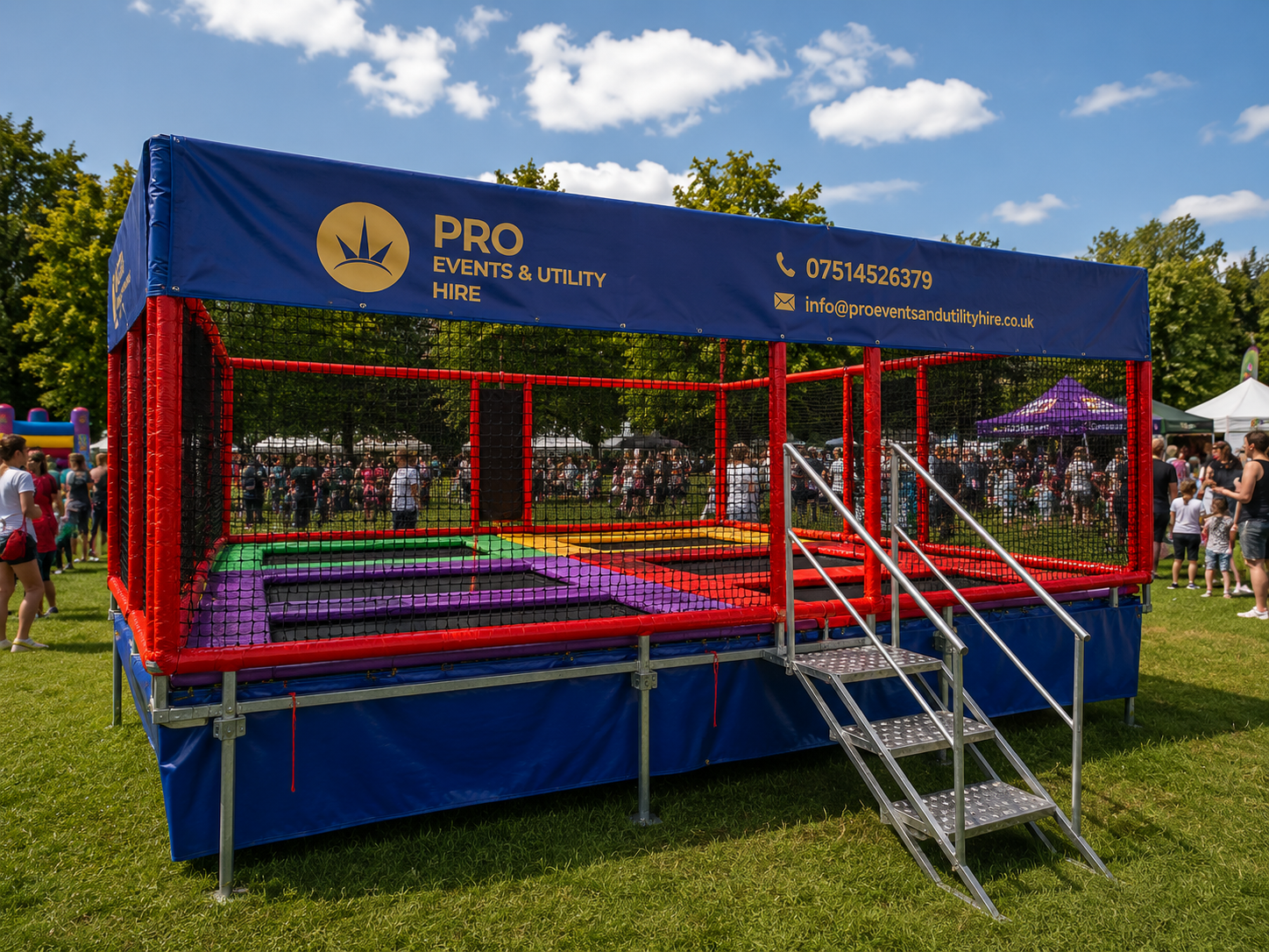 Blue-and-red outdoor trampoline with netting and a canopy at a park, with metal steps in front