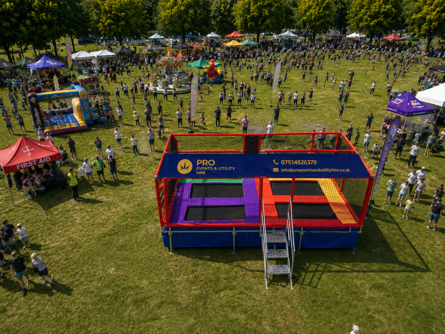 Outdoor festival field with a red-and-blue stage booth and a crowd of people scattered across the grass.