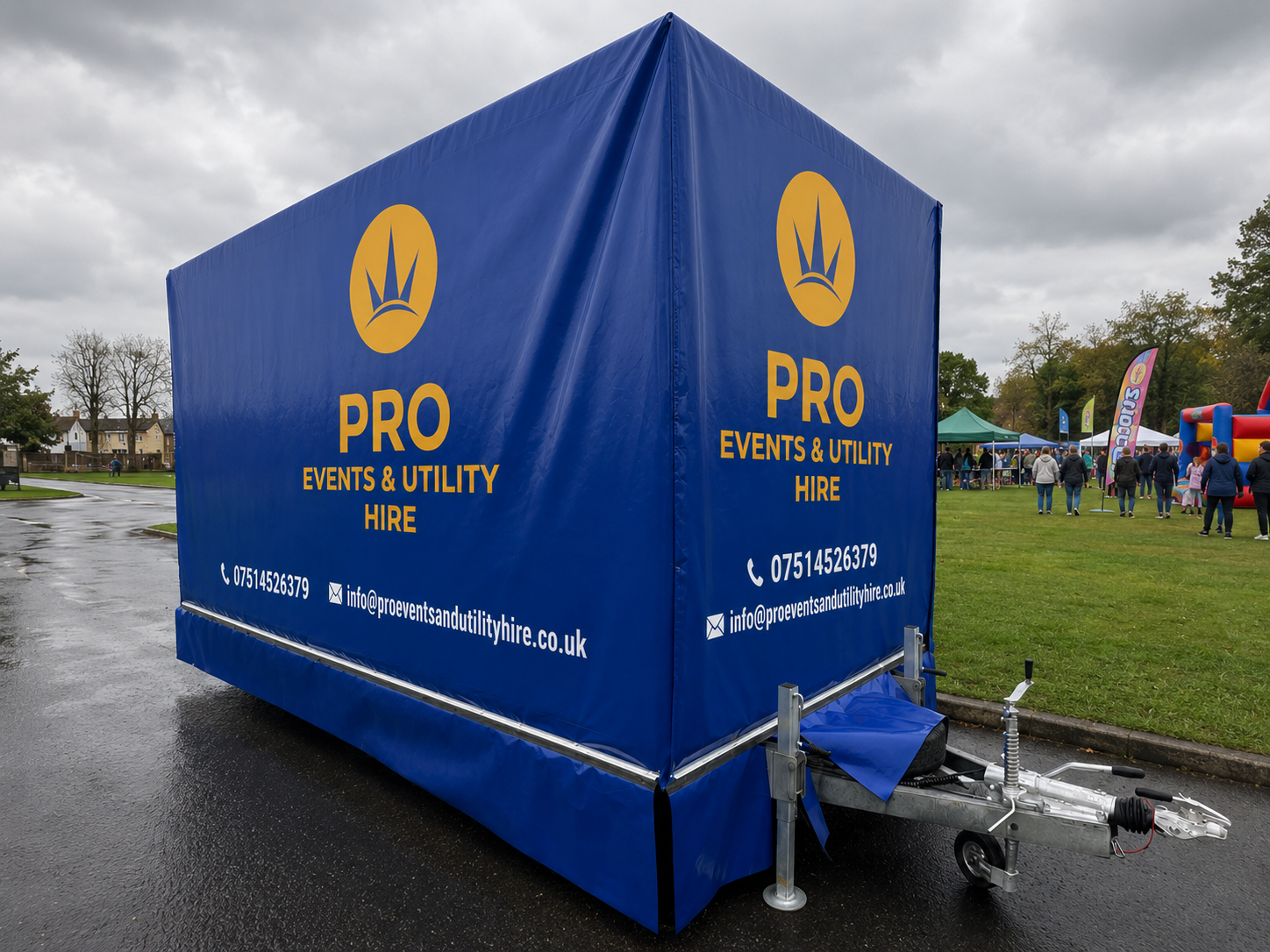 Blue PRO tent trailer on a wet road at an outdoor event, with people and flags in the background.