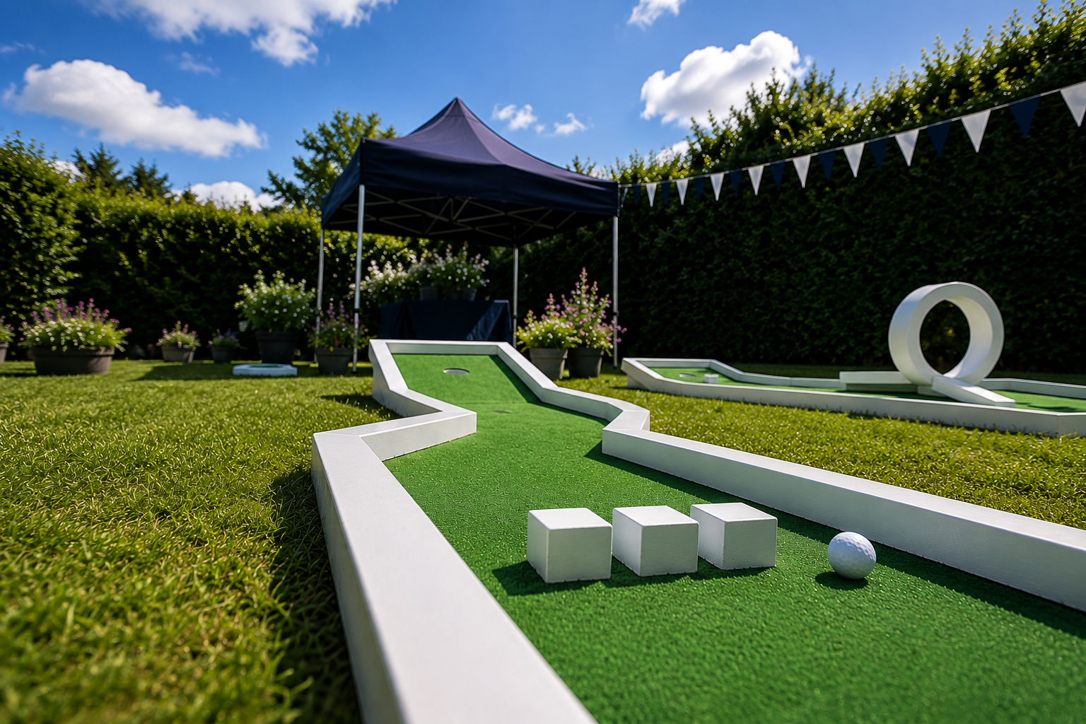 Outdoor mini golf course with green turf, white borders, a black canopy, and white bunting under a blue sky