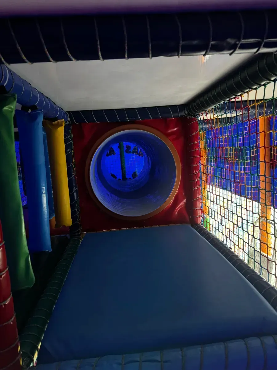 Colorful indoor play tunnel with a blue padded floor and a circular blue opening ahead