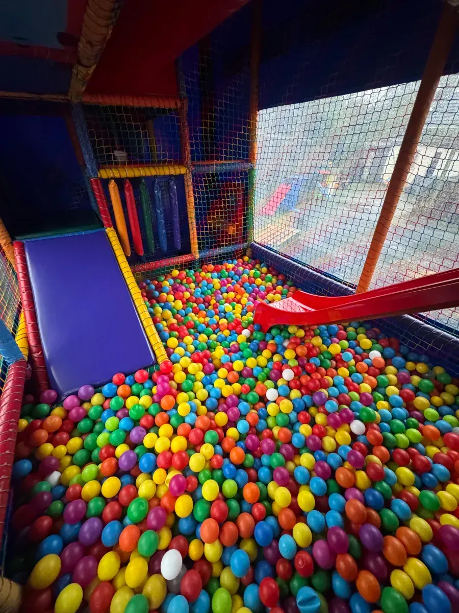 Indoor ball pit with colorful plastic balls, a blue slide, and netted play area.