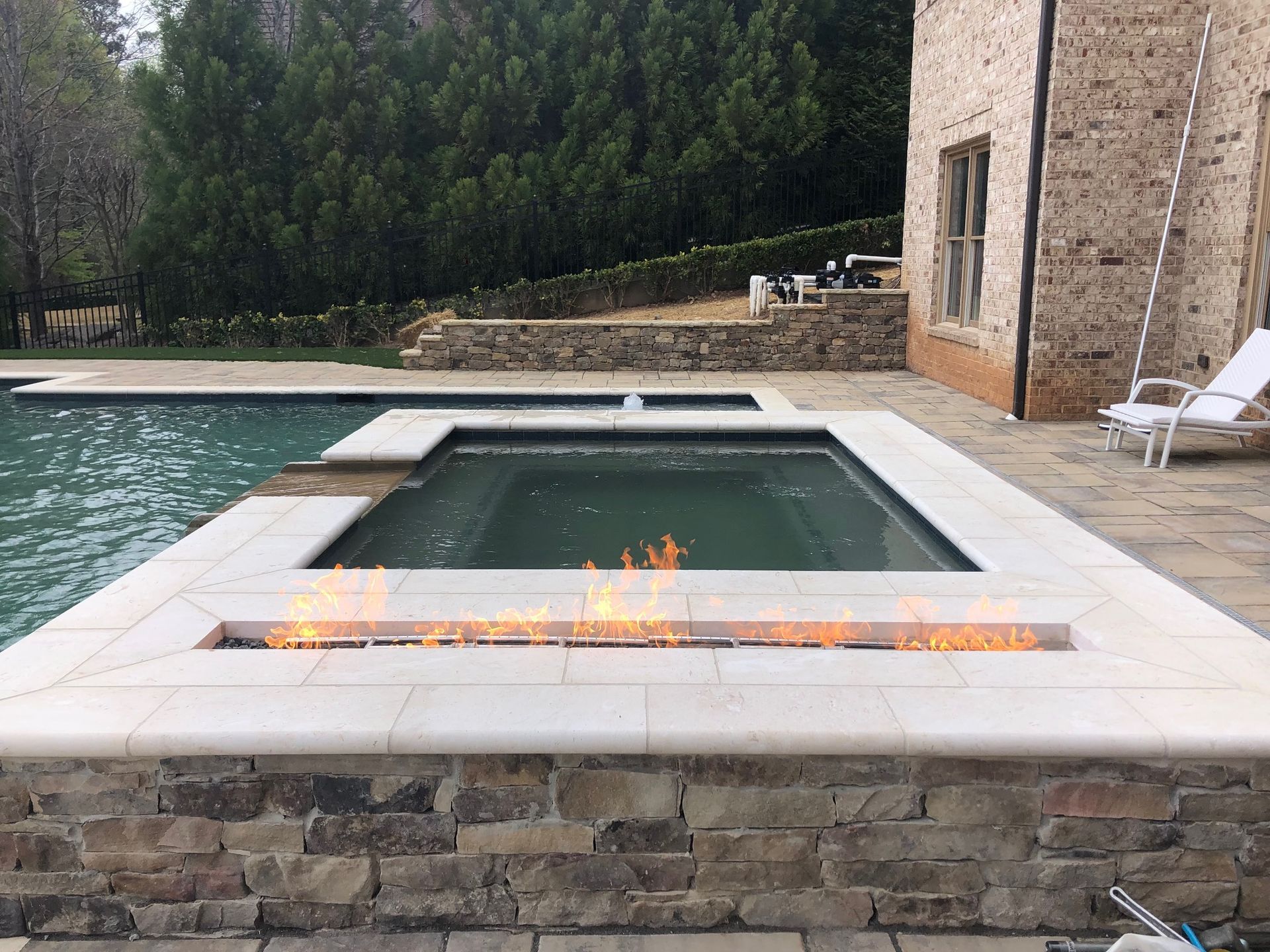 Backyard pool with a small fire feature, stone patio, and lounge chairs beside a house