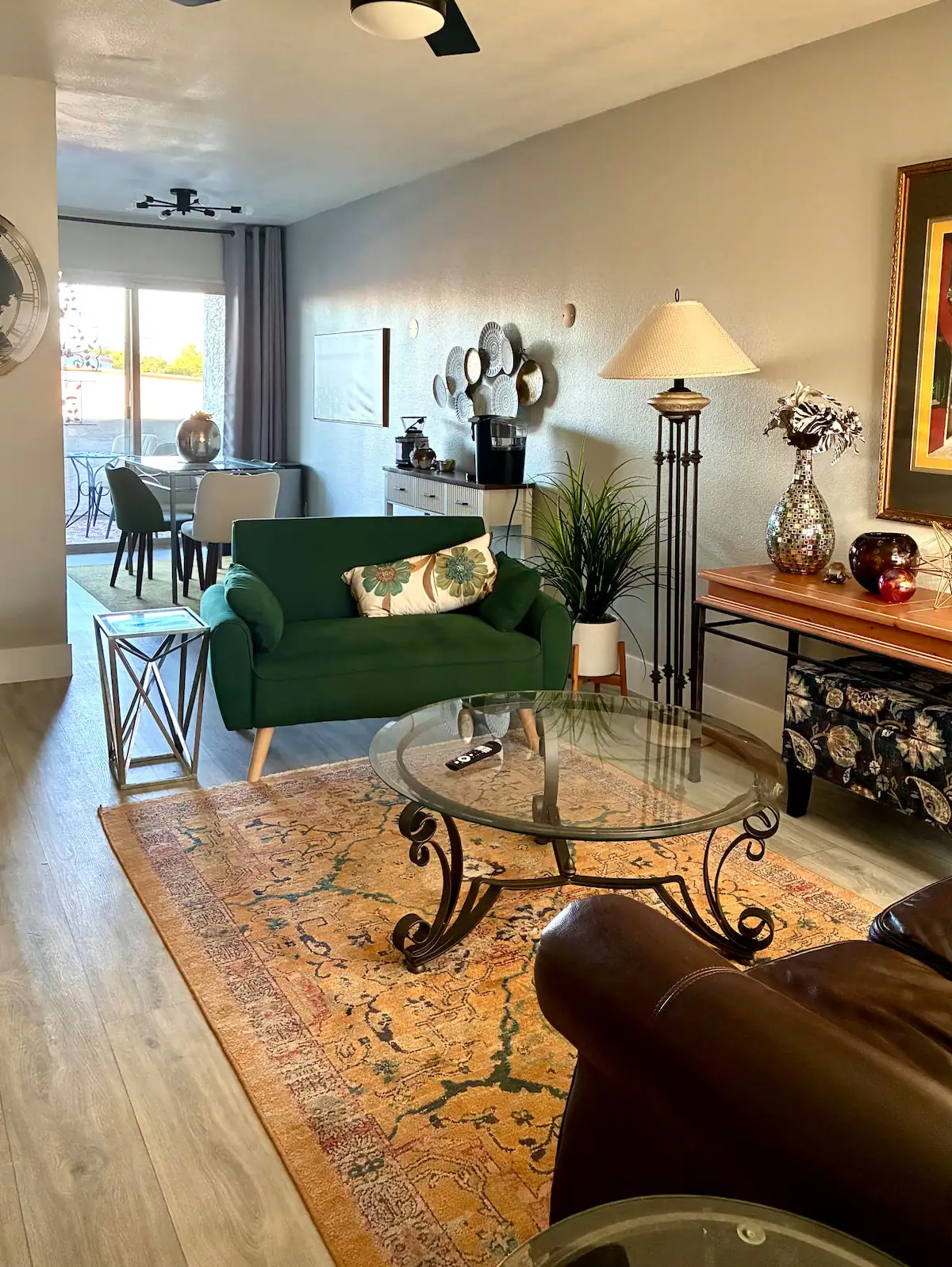 Cozy living room with green sofa, glass coffee table, patterned rug, lamp, and dining area by the window