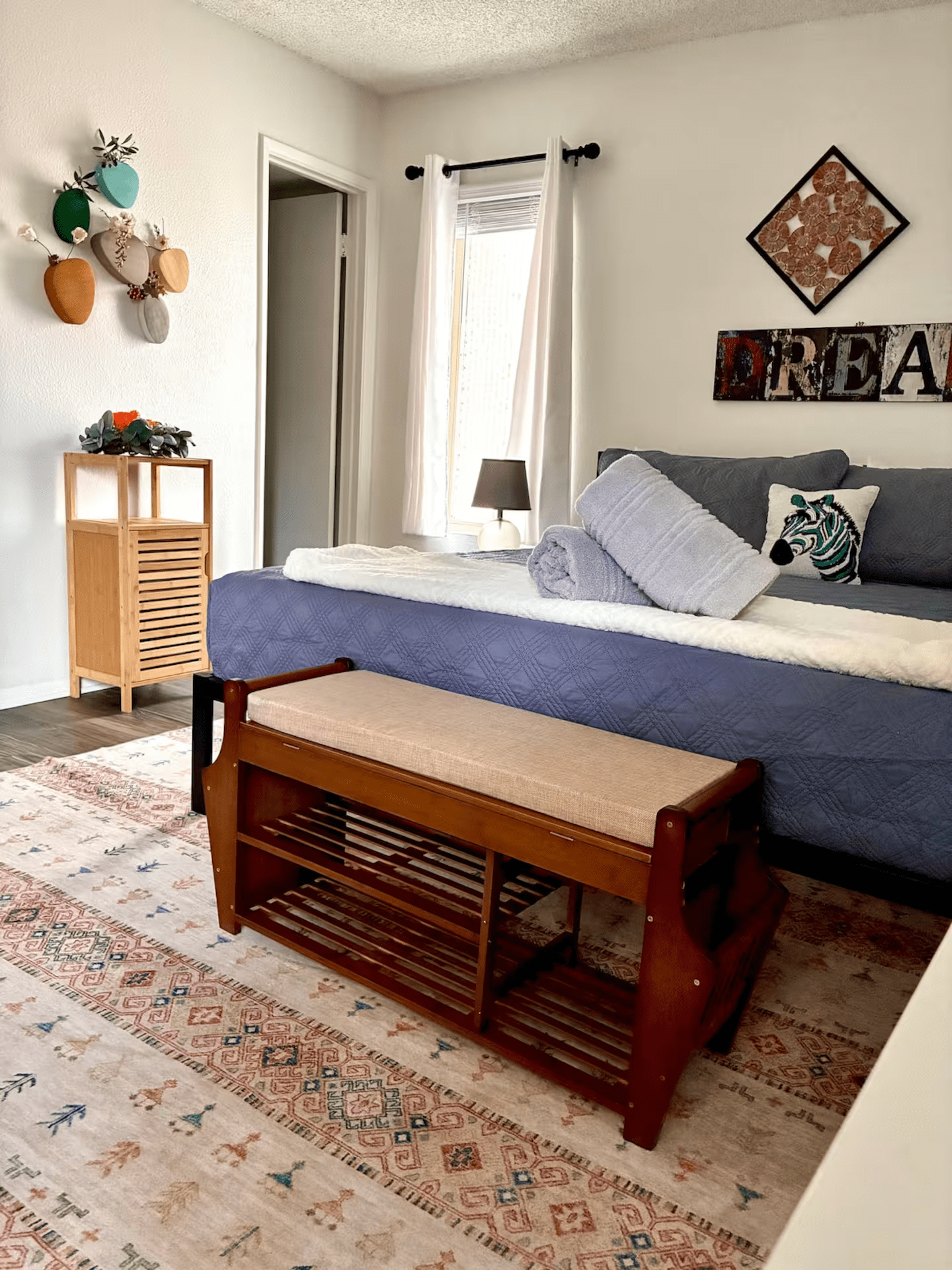 Bright bedroom with blue bed, patterned rug, wooden coffee table, and wall decor by a window