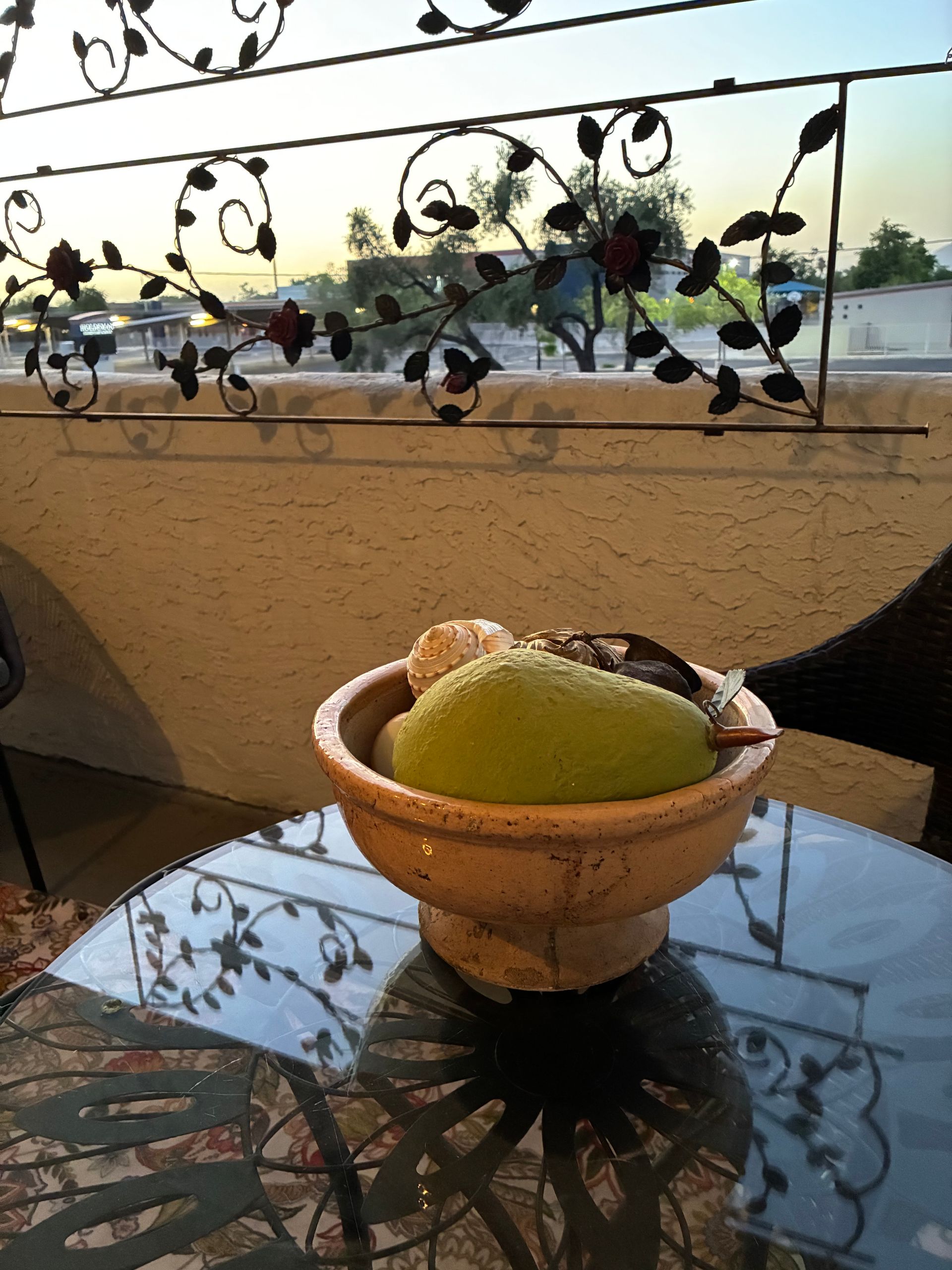 Bowl of green sorbet on a glass table, with sunset view and decorative iron railing in the background